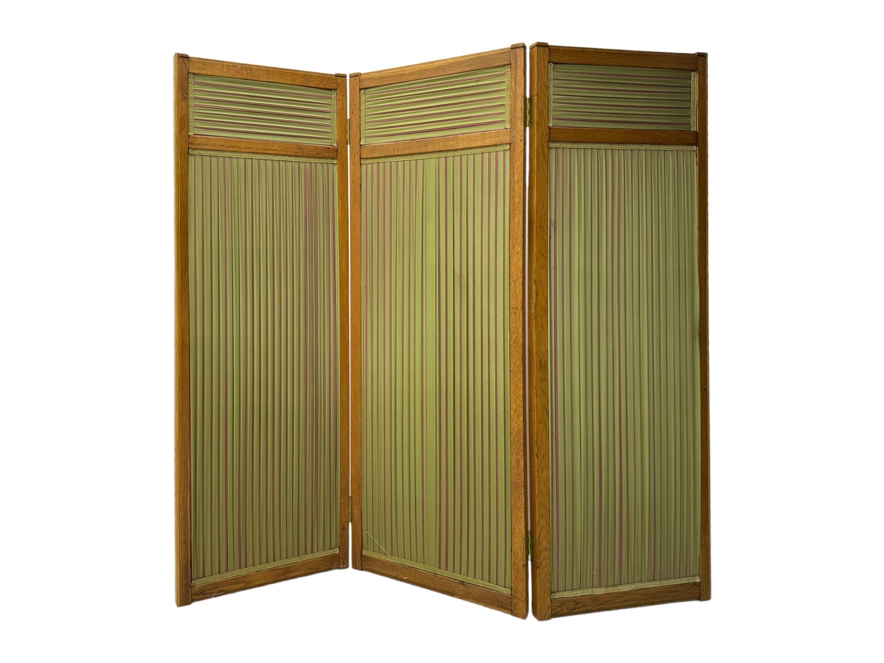 Edwardian oak and fabric folding screen, featuring three panels with oak frames, one side covered in green striped fabric with decorative trim, the reverse side in pink moiré effect fabric, connected by brass hinges