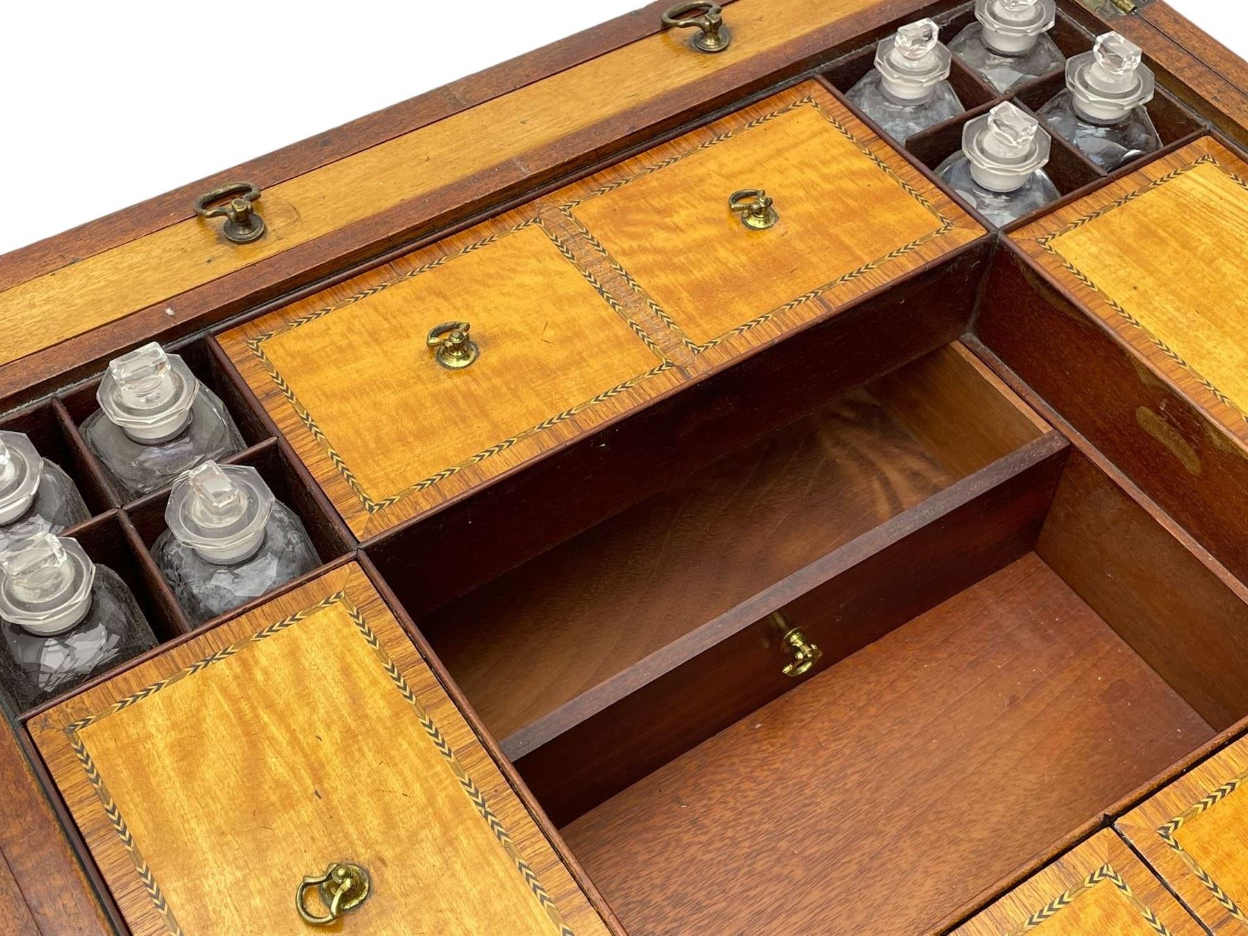 Late 19th century mahogany and satinwood dressing chest, the raised middle section hinges to reveal an interior fitted with lidded compartments, removable tray, single drawer and glass scent bottles, lift-up bevelled mirror with adjustable hinged mechanism, fitted with a further eight cock-beaded graduating drawers and curved kneehole with double cupboard, square tapering supports on brass cups and castors, inlaid throughout with checkered stringing, ornate Rococo cast gilt metal handles