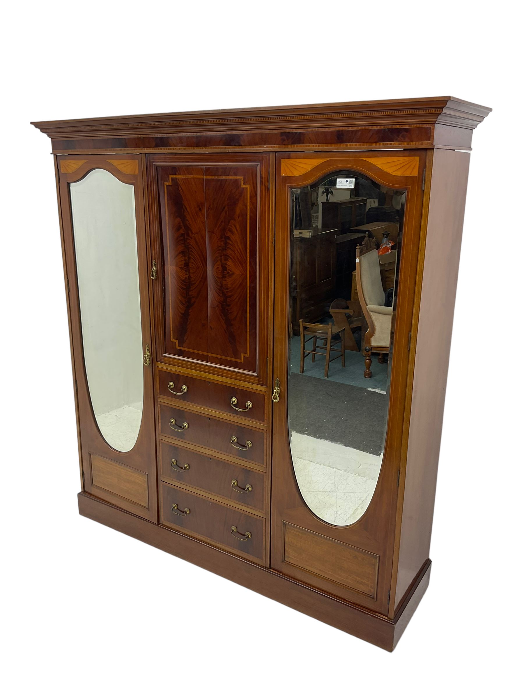 Edwardian inlaid mahogany combination wardrobe, projecting moulded cornice over figured frieze with satinwood banding, the central section fitted with cupboard over four long drawers, figured matched veneers and satinwood bands, flanked by two full height compartments enclosed by bevelled shield shaped mirror doors, satinwood fan inlaid spandrels, on moulded skirt base 