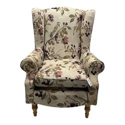 Hardwood-framed wingback armchair, upholstered in cream floral pattern fabric, on turned front feet