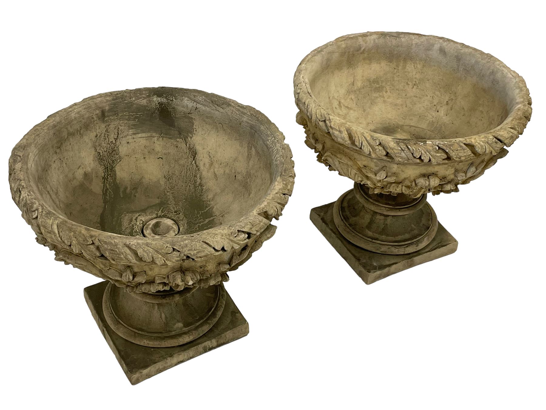 Pair of composite stone garden urn planters, acanthus leaf garland rim over foliate decorated body, stepped foot on square base