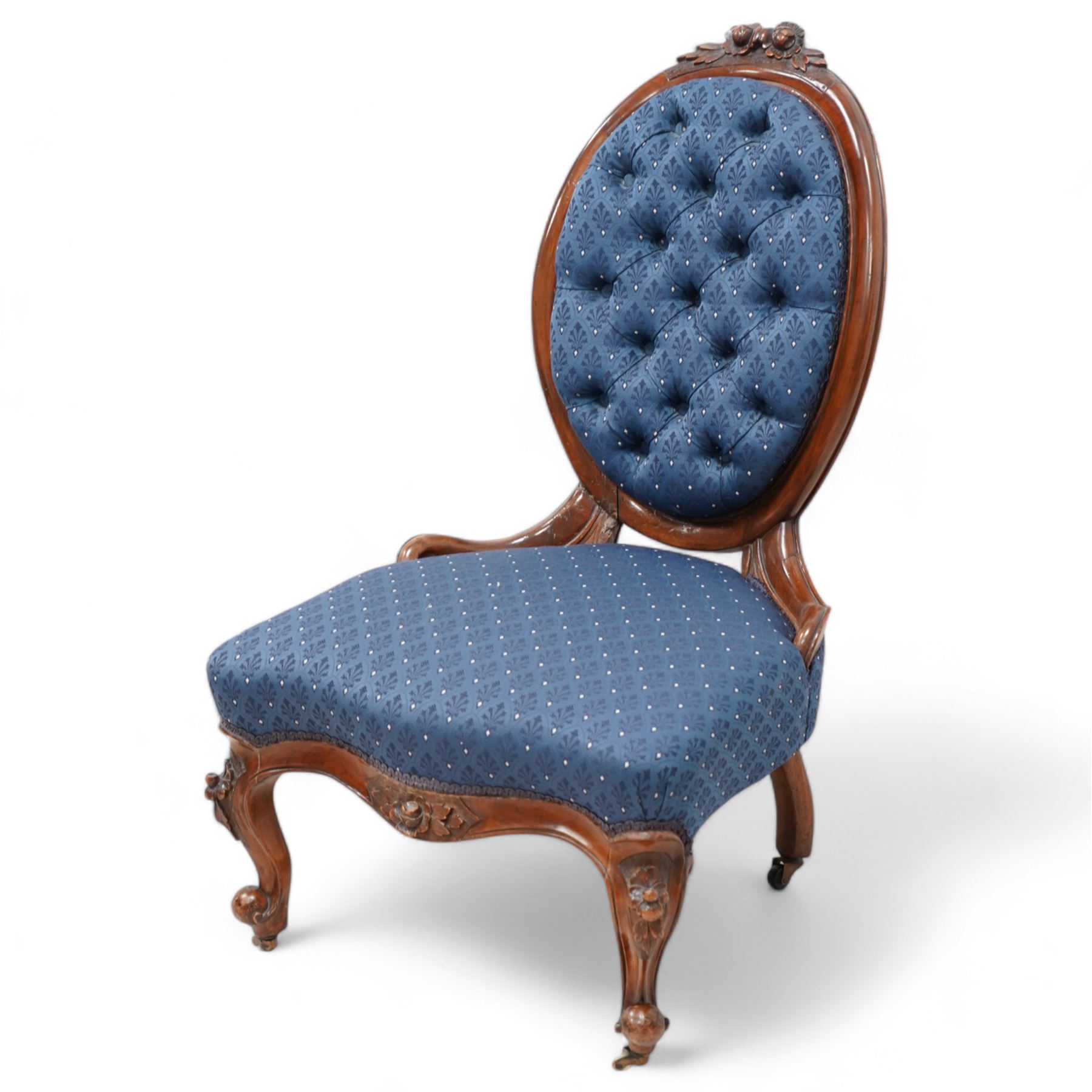 Victorian carved walnut framed nursing chair, the cresting carved with flower heads and extending foliage, upholstered in buttoned blue fabric with repeating pattern, on floral carved cabriole feet