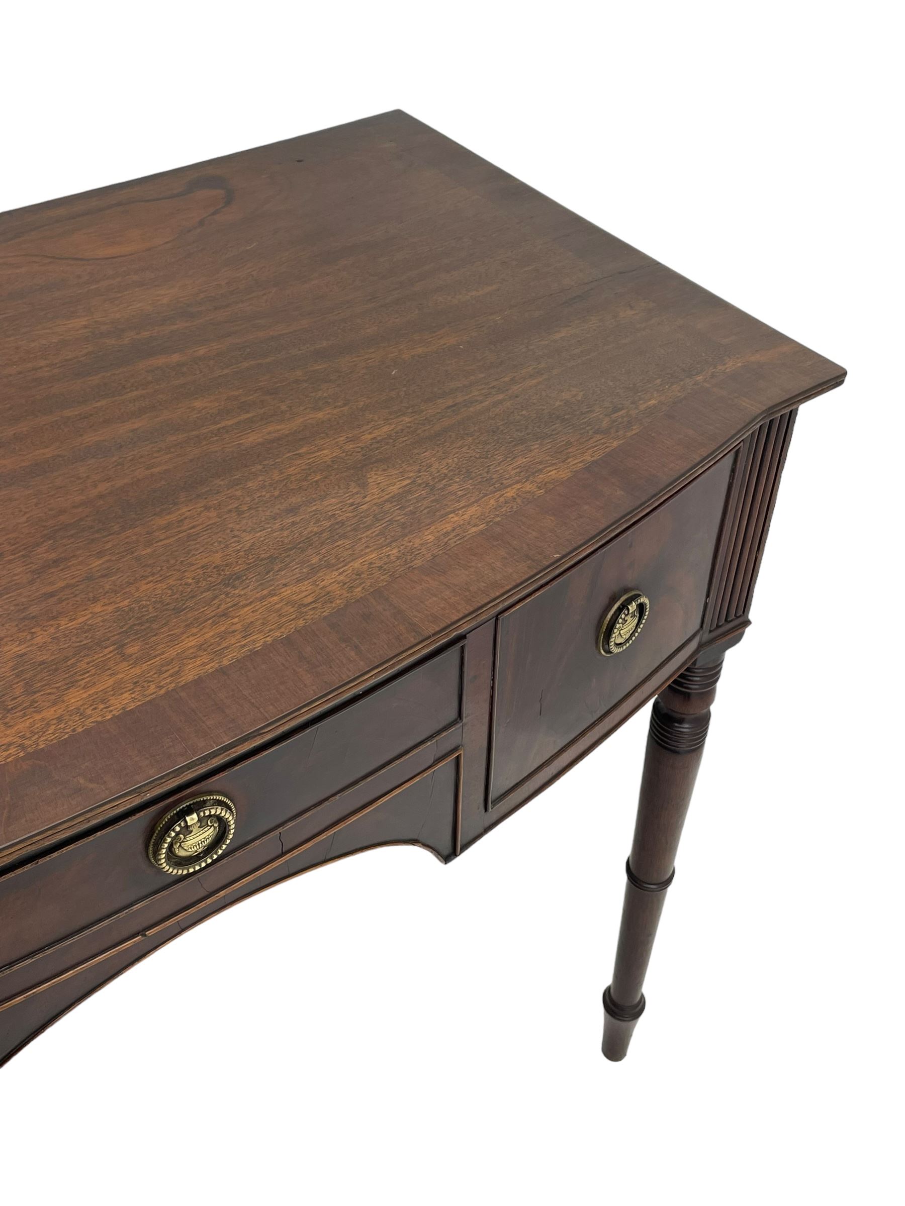 George III mahogany kneehole dressing or writing table, stepped bow-front form, reed moulded top with mahogany crossband, fitted with three cock-beaded drawers with circular pressed brass handle plates decorated with urn and beaded ring handle, on ring turned supports 