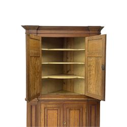 George III and later oak and mahogany banded corner cupboard, moulded cornice over four panelled doors, the door panels inlaid with mahogany bands, projecting square pilasters throughout with applied reeded mouldings, the painted interior fitted with shaped shelves, on moulded plinth base 