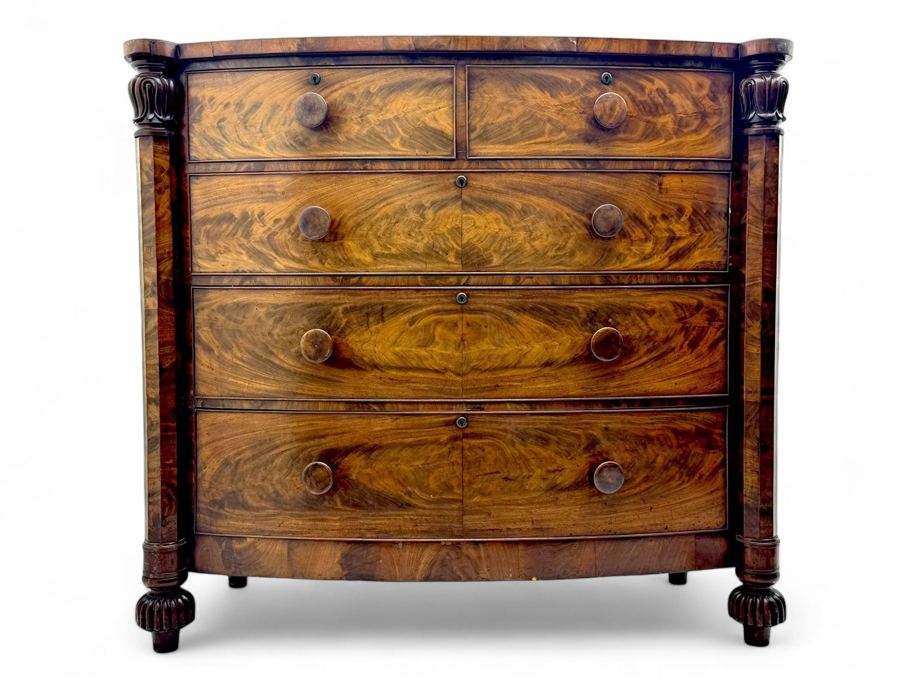 Early Victorian mahogany bow front chest, two short over three long graduating cockbeaded drawers, flanked by faceted columns with carved acanthus leaf capitals, standing on turned bun supports with fluted detailing