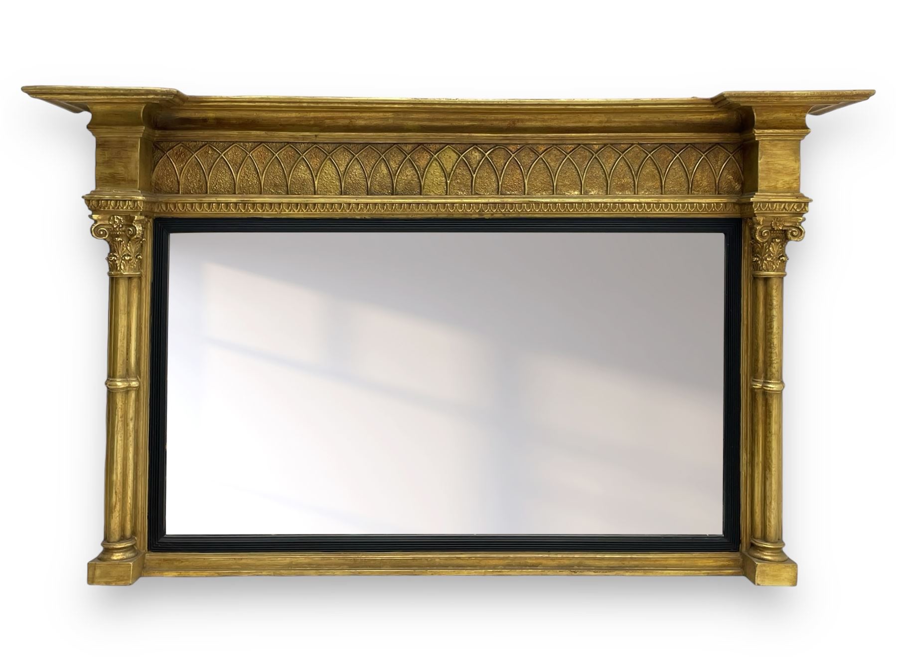 Regency design giltwood overmantel mirror, projecting cornice over pointed arcade frieze and foliate moulded upper edge, plain mirror plate within reed moulded ebonised slip, flanked by cluster columns with acanthus and scroll decorated Composite order capitals 