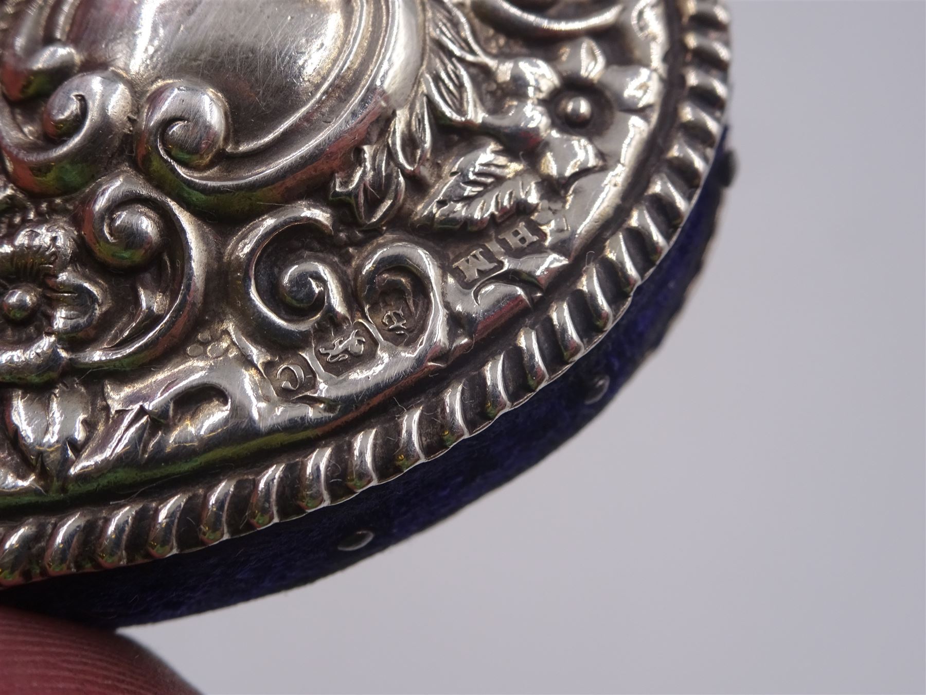 Edwardian silver pin cushion, in the form of a heart, with embossed floral decoration, with blue pin cushion between two heart shaped silver covers, with chatelain hook, hallmarked Henry Matthews, Birmingham 1902, together with a late Victorian silver thimble holder, embossed with scrolling decoration and with velvet interior, with chatelain chain, hallmarked Levi & Salaman, Birmingham 1899, pin cushion H4.5cm