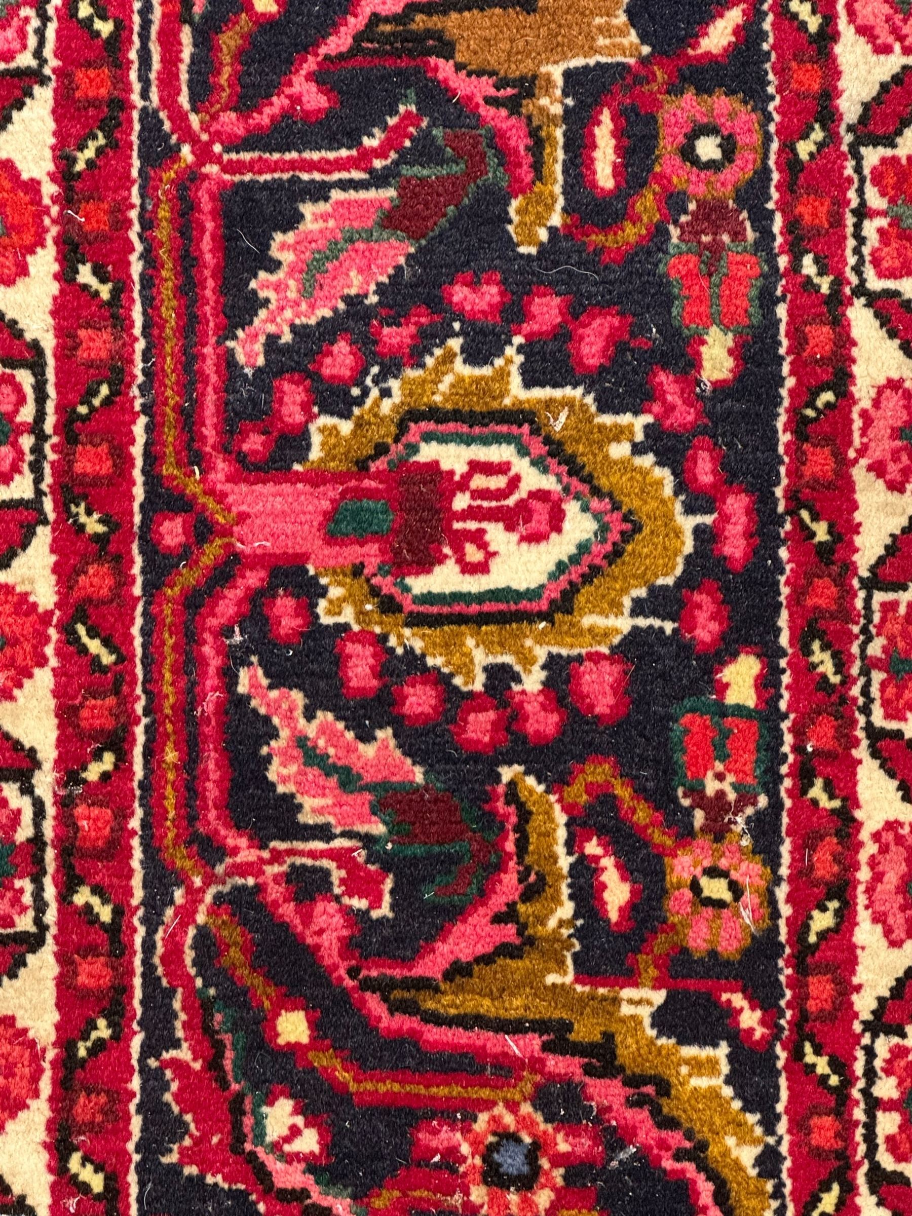 Persian Nanaj crimson ground carpet, the busy field filled with interconnecting stylised plant motifs with scrolling branches, the guarded indigo border decorated with repeating palmettes and foliate patterns