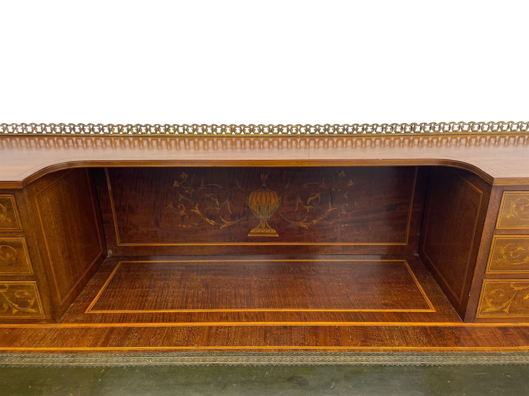 Edwardian inlaid mahogany writing desk, raised galleried back over inlaid central urn with scrolling leafy branches and six small drawers, satinwood banded rectangular moulded top with tooled leather inset, fitted with five drawers, the drawer facias inlaid with scrolling foliage and satinwood banding, square tapering supports inlaid with trailing bell flowers, on brass and ceramic castors 