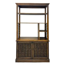 Mid 20th century oak bookcase cupboard, projecting cornice over three open shelves with subdivided sections and latticework uprights, two doors to the base with floral and scrollwork carvings and central brass handles, resting on a moulded plinth base