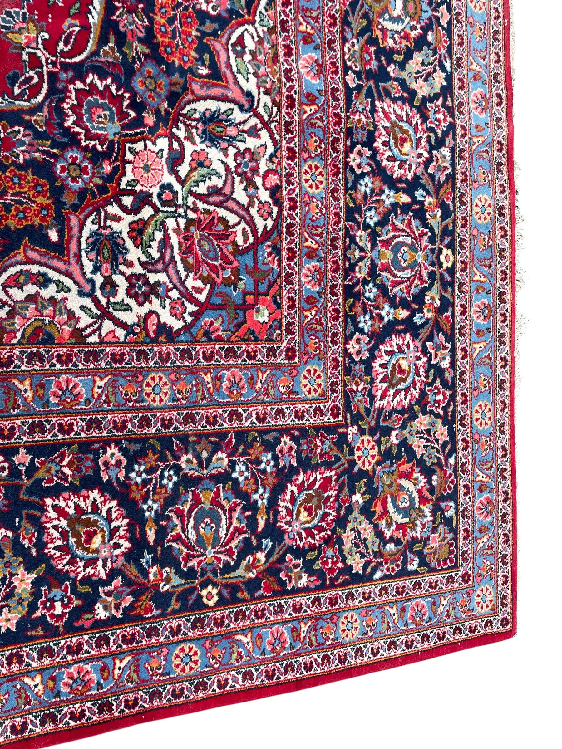 Large Persian Kashan crimson ground carpet, central floral medallion surrounded by swirling leafy branches and palmettes, enclose by floral pattern spandrels, the indigo border with overall scrolling design decorated with palmettes, within guard stripes 