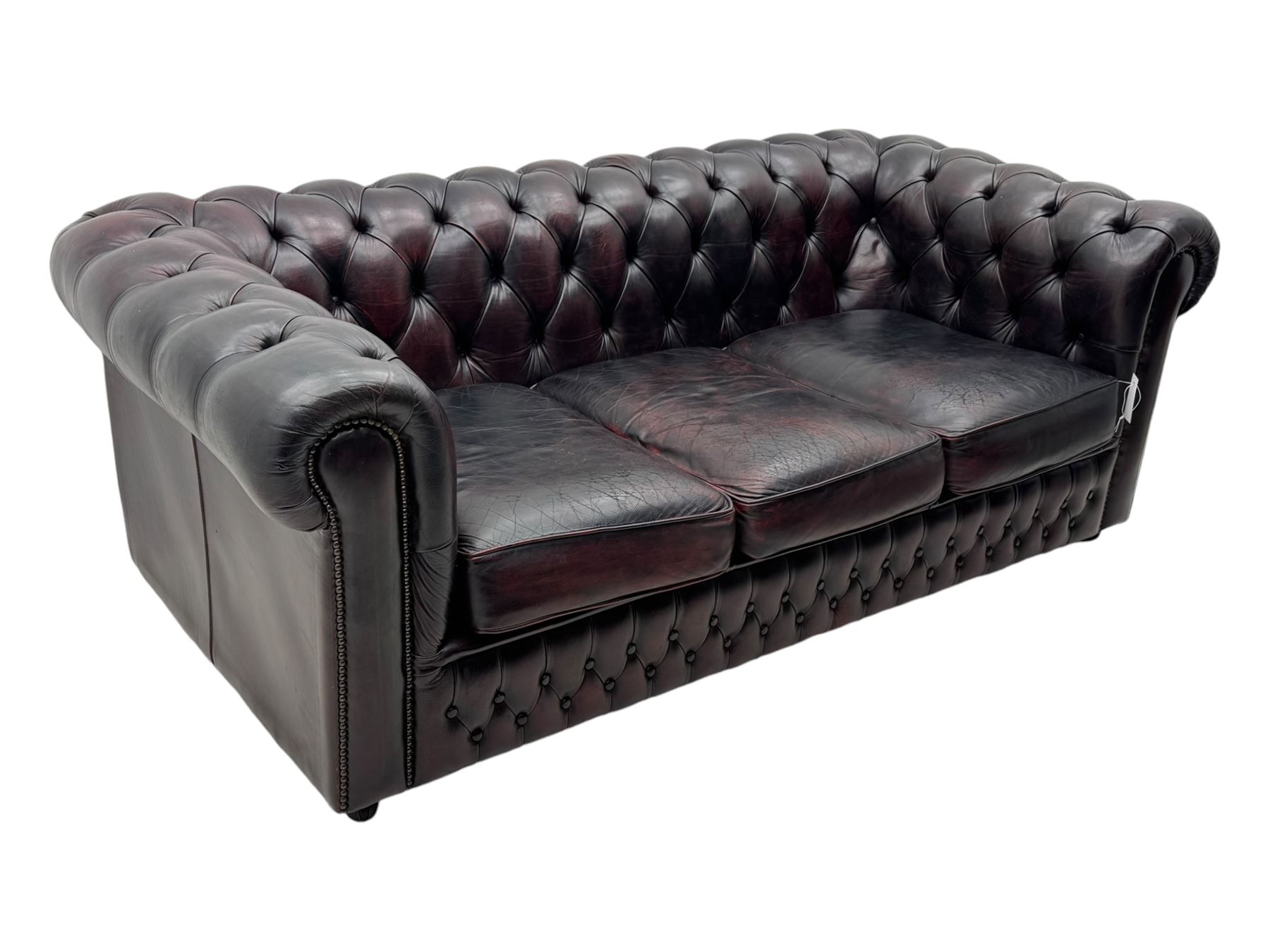 Chesterfield three-seat sofa, traditional shaped upholstered in deeply buttoned dark red leather; together with similar footstool 