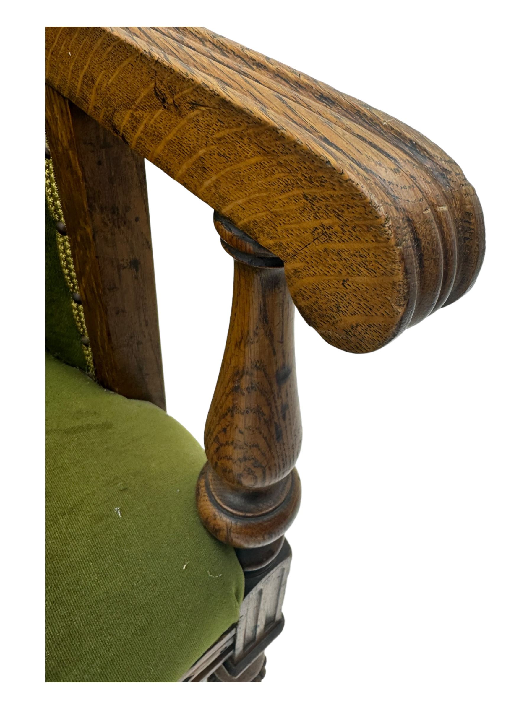 Late Victorian walnut framed sofa, rectangular backrest with carved detailing and central motif, upholstered in olive green fabric with brass studded trim and patterned front rail, scrolled fluted arms supported by turned uprights terminating in bun feet