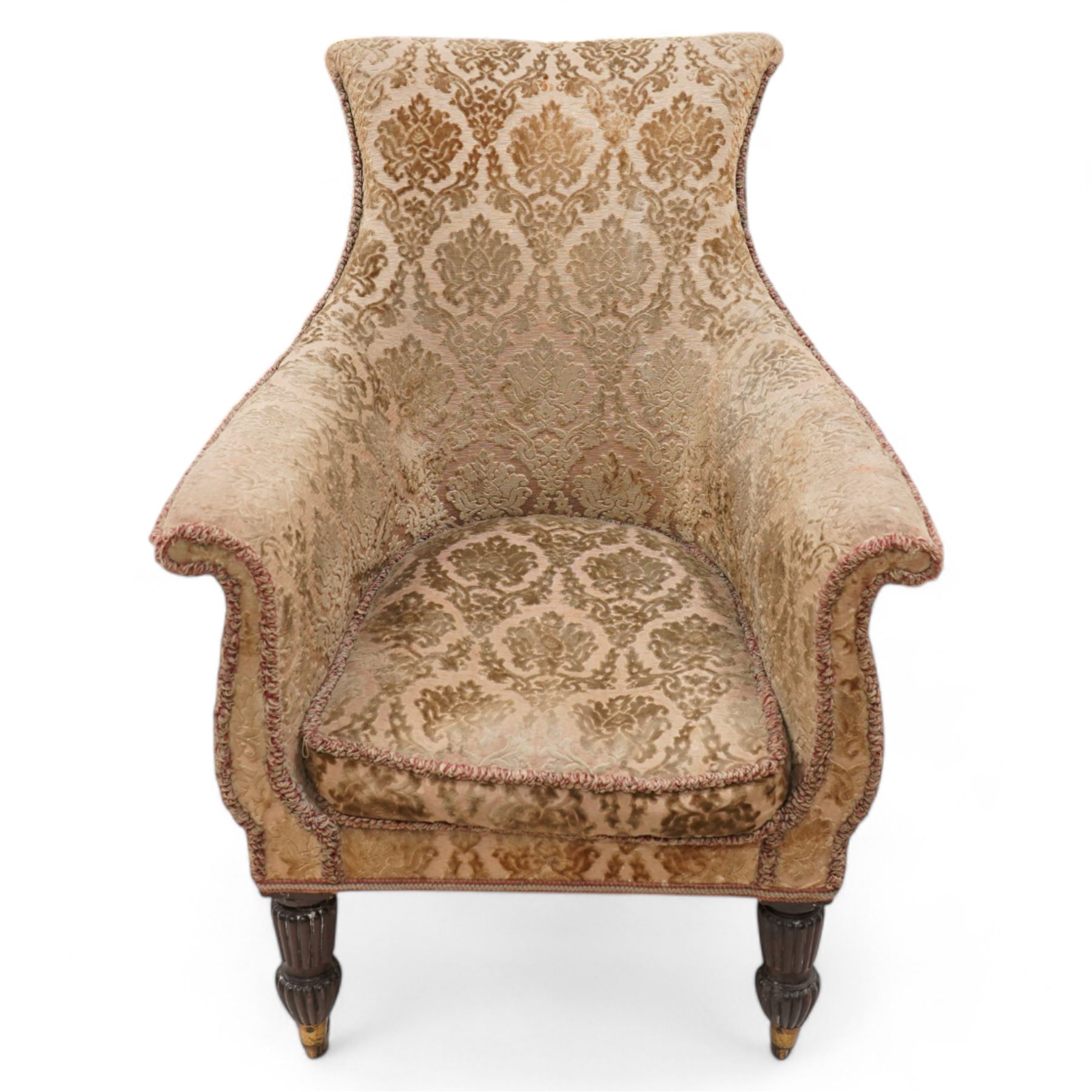 Early 19th century mahogany framed armchair, curved form with rolled cresting, upholstered in raised foliate pattern fabric, tub seat with shaped and rolled arms, on turned and reed carved front feet, brass cups and castors 