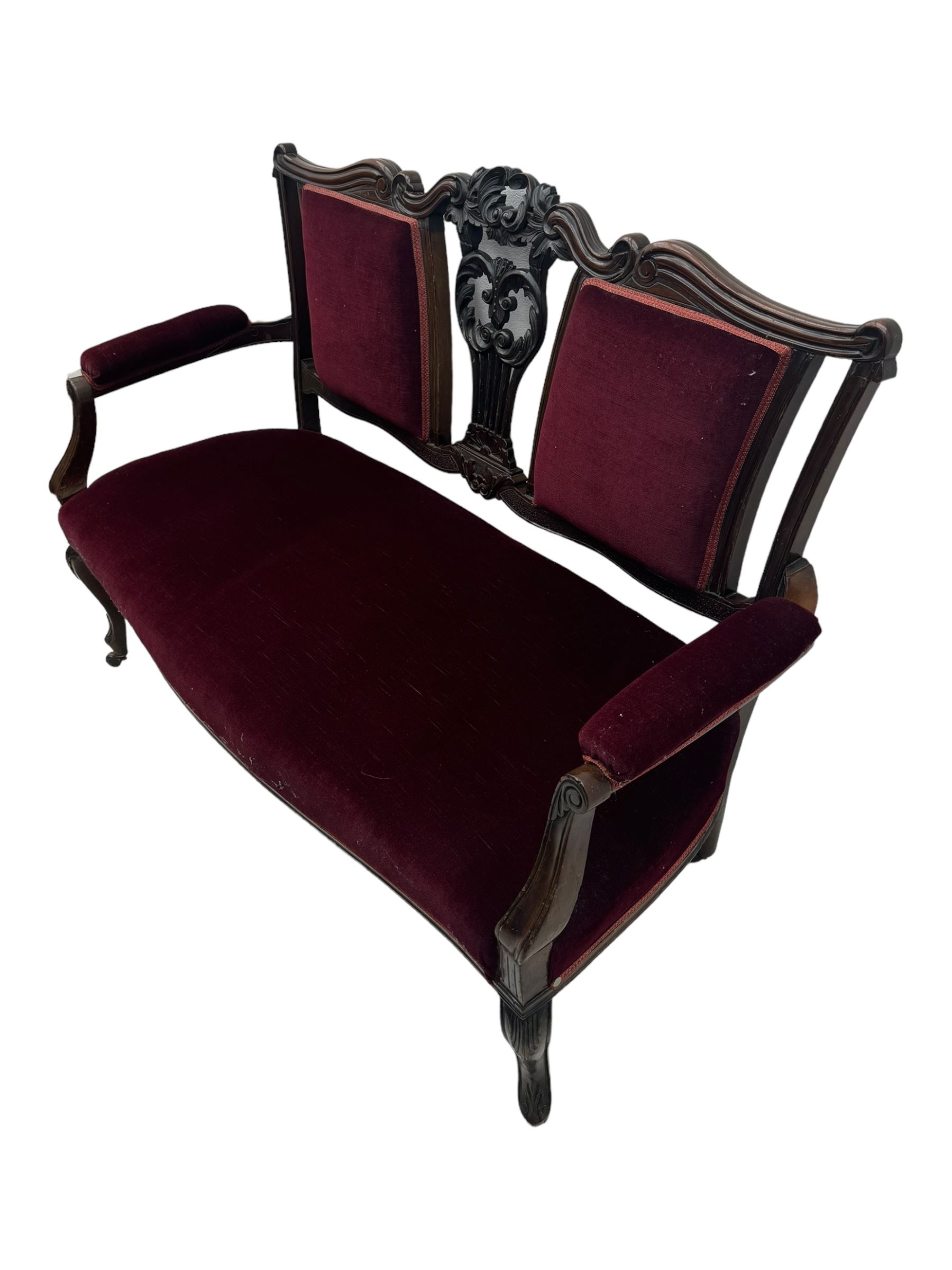 Late Victorian dark oak framed sofa, the backrests, seat and padded arms upholstered in deep red fabric, carved crest rail with scroll and foliate motifs supported by carved uprights, on cabriole supports with leaf carvings terminating in castors