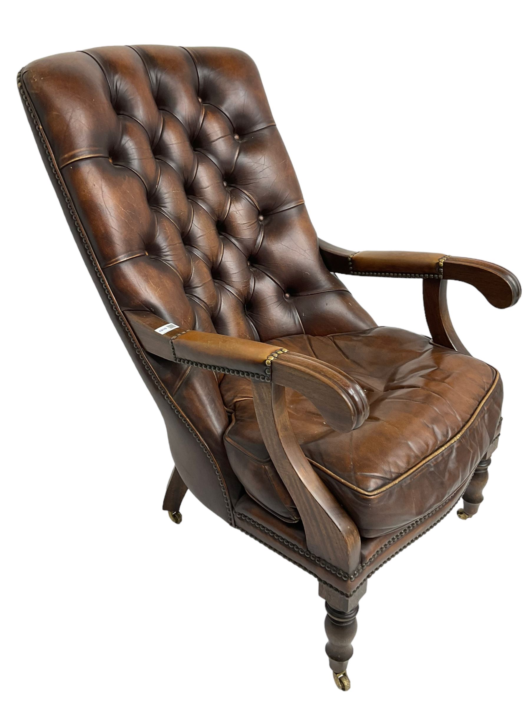 Georgian design mahogany framed library armchair, upholstered in buttoned chocolate brown leather with studwork and loose seat cushion, raised on turned supports with brass castors