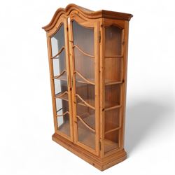 Polished pine display cabinet, shaped top over two glazed doors, fitted with three shelves, on moulded plinth base 