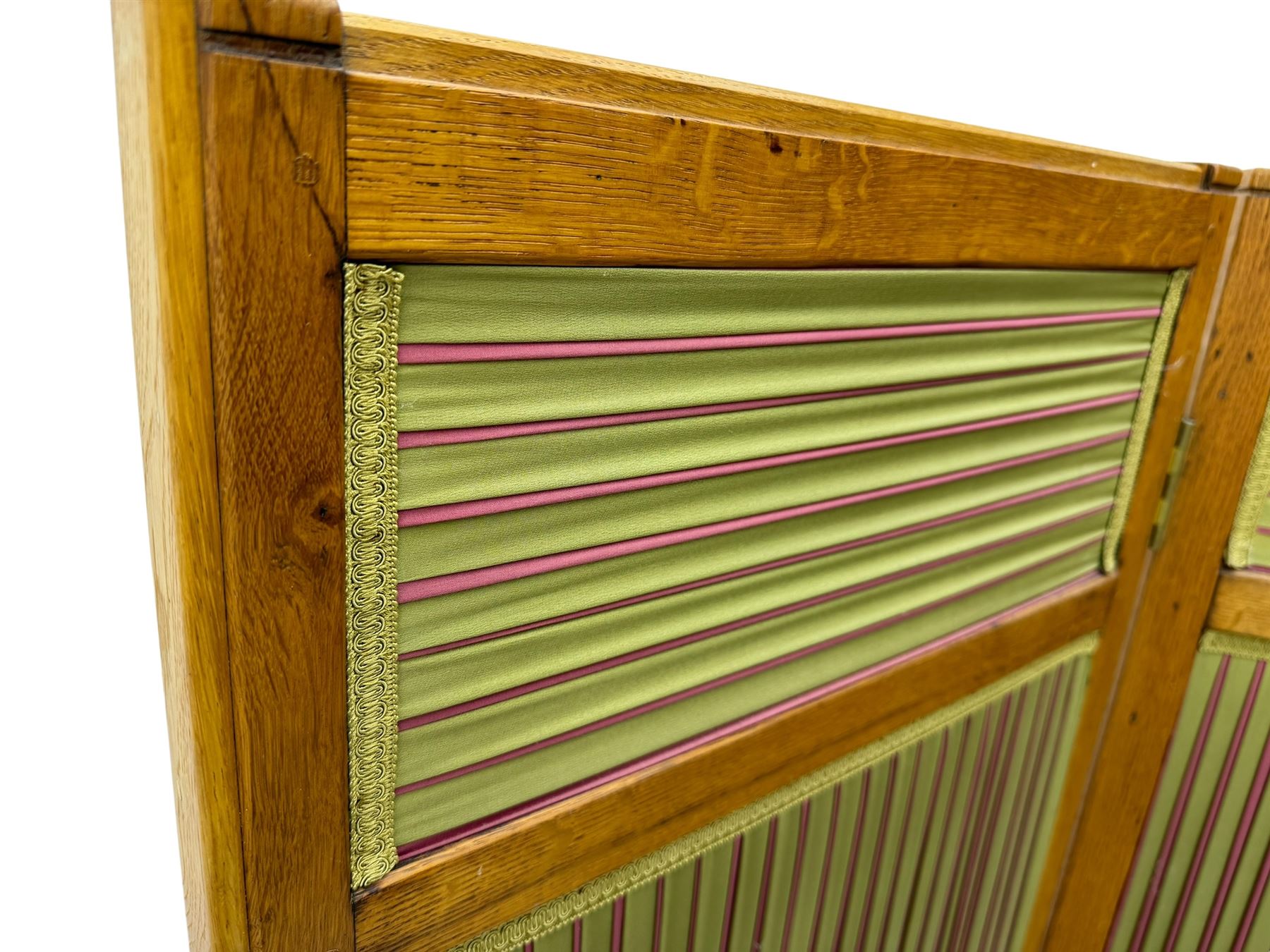 Edwardian oak and fabric folding screen, featuring three panels with oak frames, one side covered in green striped fabric with decorative trim, the reverse side in pink moiré effect fabric, connected by brass hinges