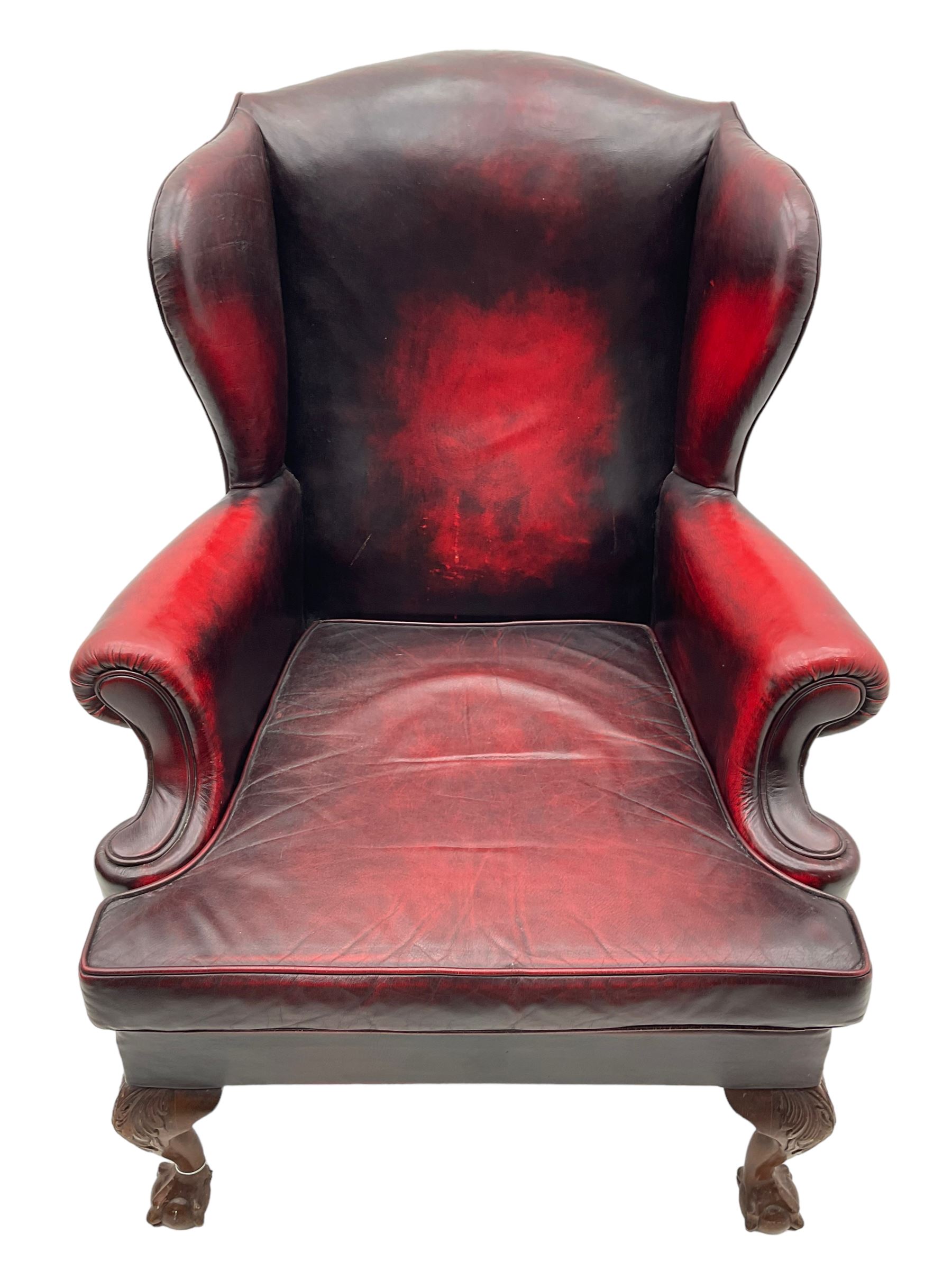 Georgian design hardwood-framed wingback armchair, upholstered in red leather, loose seat cushion and rolled arms, on acanthus carved ball and claw front feet 