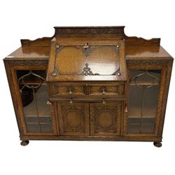 Early 20th century heavily carved oak bookcase bureau, raised back with grape-vine carved frieze, over fall-front enclosing fitted interior, above two short drawers and curved frieze drawer, flanked by astragal glazed and panelled cupboards, on turned feet