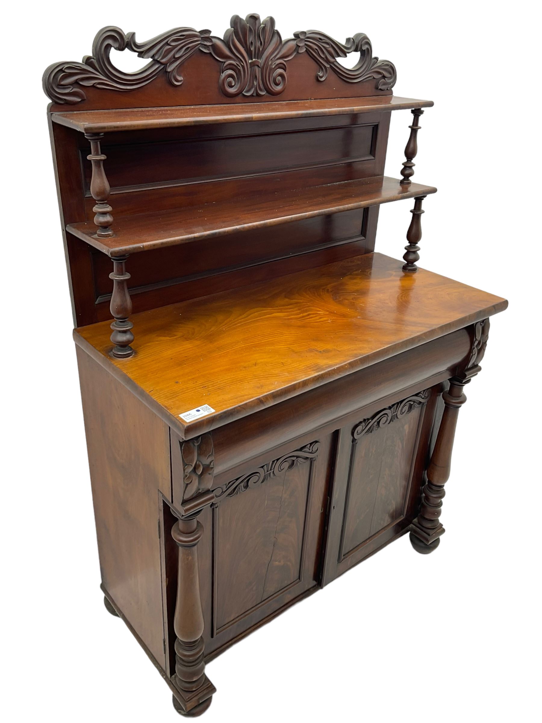 Victorian mahogany chiffonier, raised shaped pediment carved with scrolled extending foliage, two graduating shelves on turned supports, rectangular top over drawer and double cupboard, turned column pilasters, on turned feet 