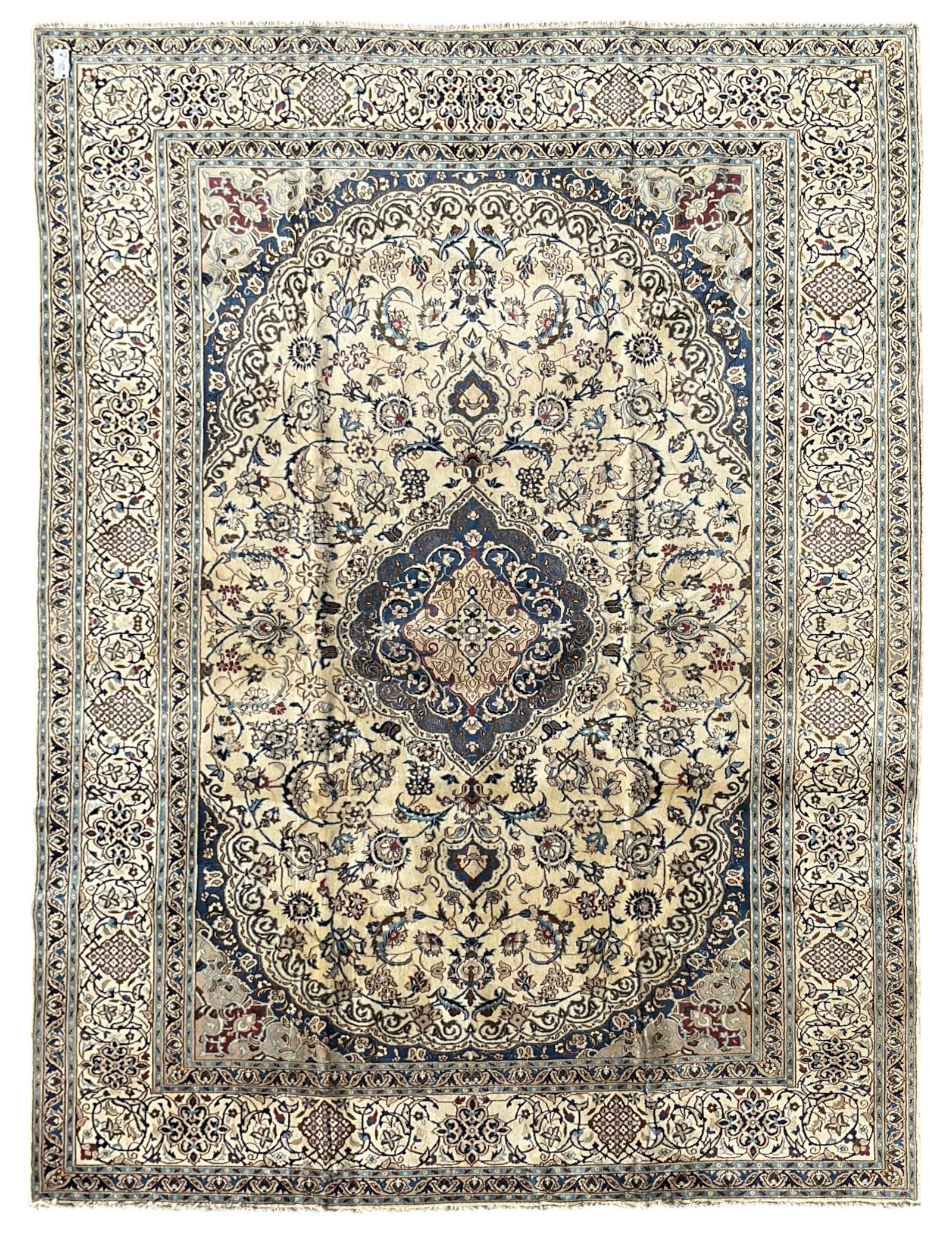 Persian Nain ivory ground carpet, central indigo medallion, the busy floral field decorated with scrolling vines and flower heads in shades of blue, beige, and red, wide guarded border with repeating palmettes and foliate motifs