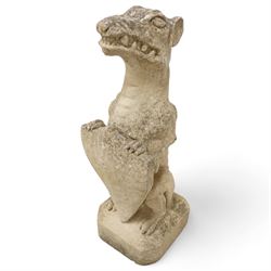 Near pair of cast stone garden seated dragons, snarling jaw holding shield on chamfered base 