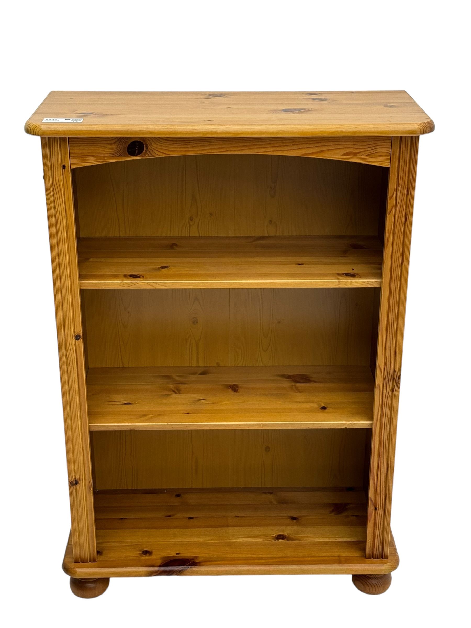 Traditional pine open bookcase, featuring arched top section flanked by fluted side supports, two adjustable shelves and cast iron coat hook with cat motif to the left side, standing on round bun feet 