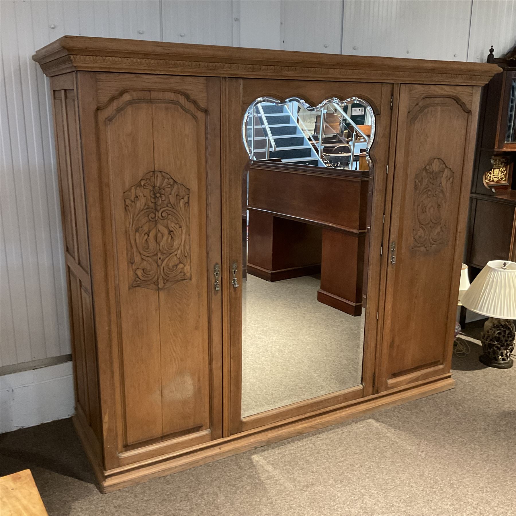 Late 19th century oak triple wardrobe, wide central bevelled mirror door, flanked by two panelled doors each carved with scrolling leaves and flower heads, on moulded skirt base 