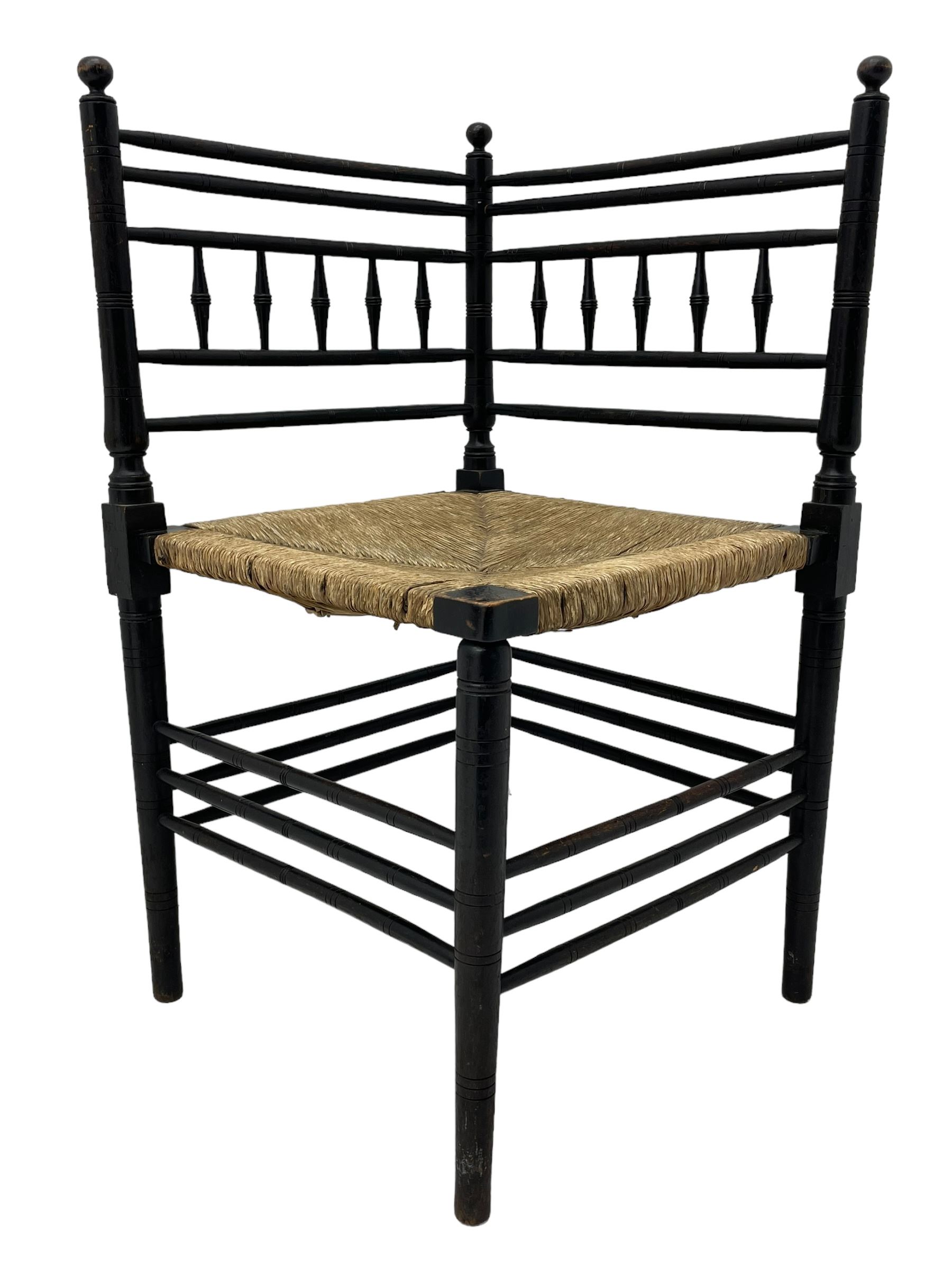 In the manner of William Morris - Arts & Crafts period corner chair, swell turned horizontal rails with balustrade back, rush seat on ring turned supports, black paint finish 