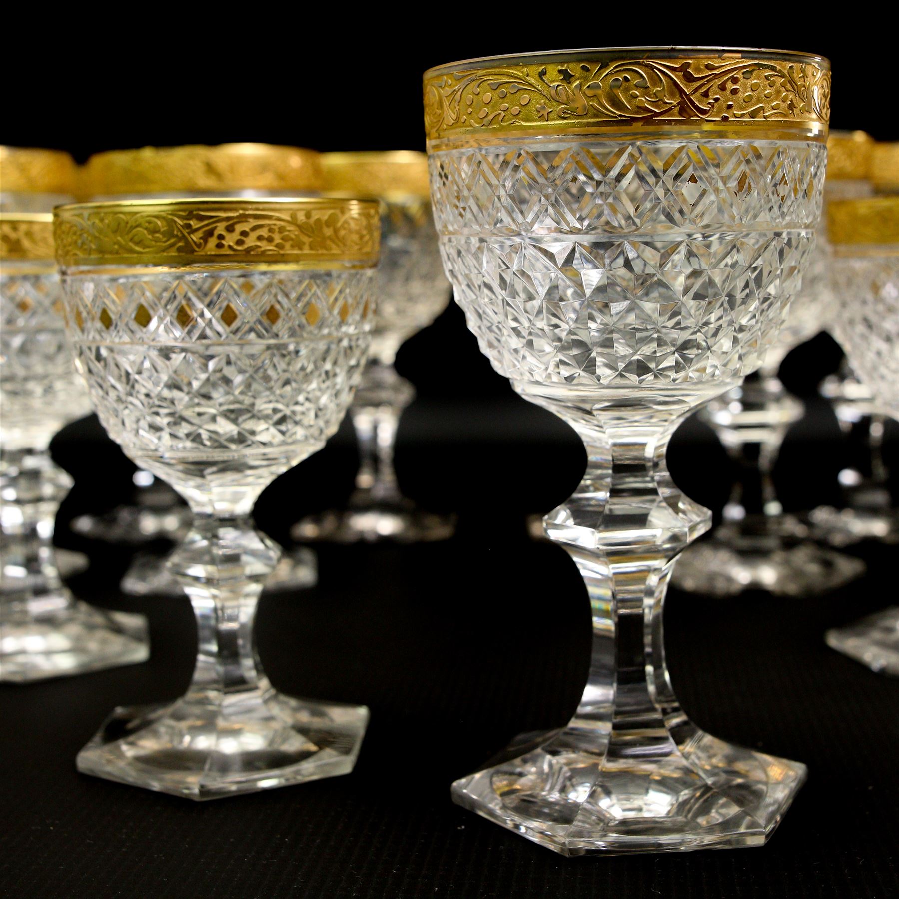 Part suite of crystal drinking glasses comprising thirteen red wine glasses and twelve white wine glasses, all with foliate gilt banding, hobnail cut bowls and hexagonal faceted stems, in the style of Moser 