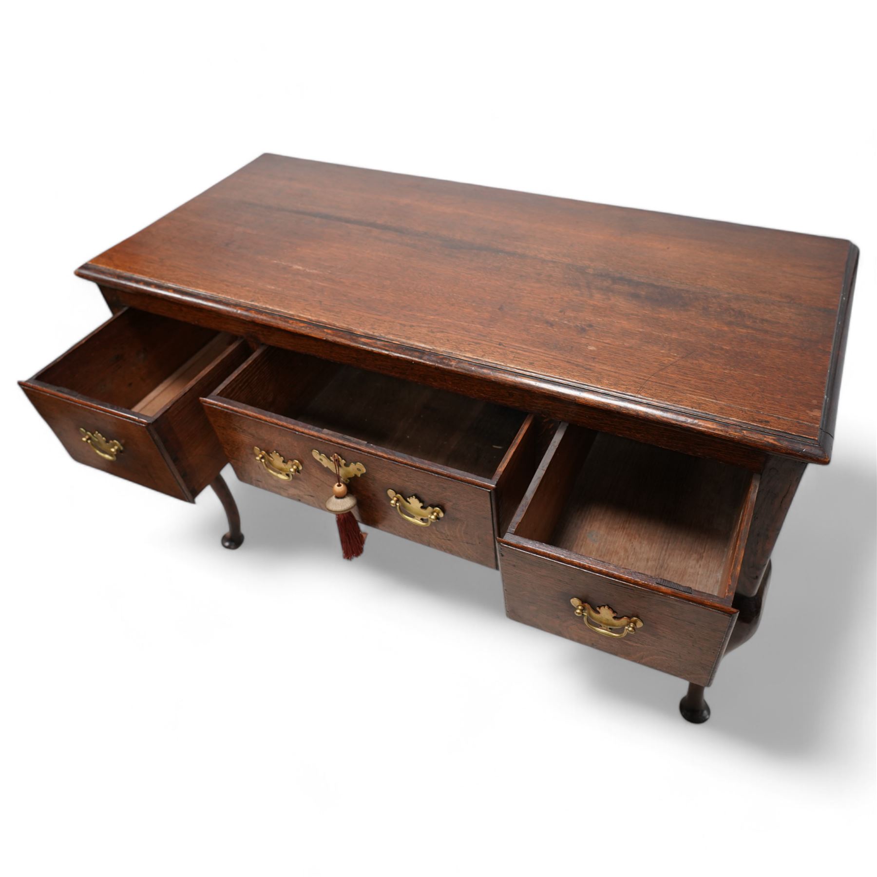 18th century oak dresser base, the rectangular top with moulded edge, fitted with three drawers with original brass handle plates, over a shaped frieze, raised on front cabriole supports with pad feet