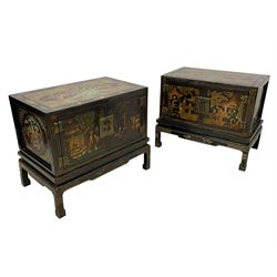 Pair of early 20th century Chinese ebonised and lacquered wood cabinets, the top decorated with dragons over lapping waves within a gilt patterned panel, the surrounding band decorated with Chinese symbols and flowerheads, enclosed by two doors each with village scenes with pagodas, figures and trees, the panelled sides decorated with a figure riding a dragon on stands with gilt decorated 