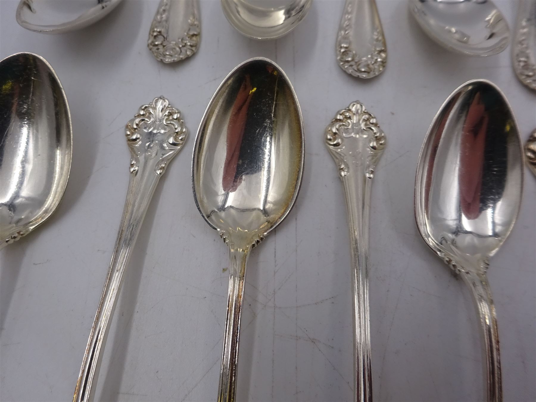 Two sets of twelve late 19th/ early 20th century American silver coffee spoons, the first set with engraved initial to terminal within scrolling border and engraved date verso, the second set with embossed floral decoration to handles, all stamped Sterling 