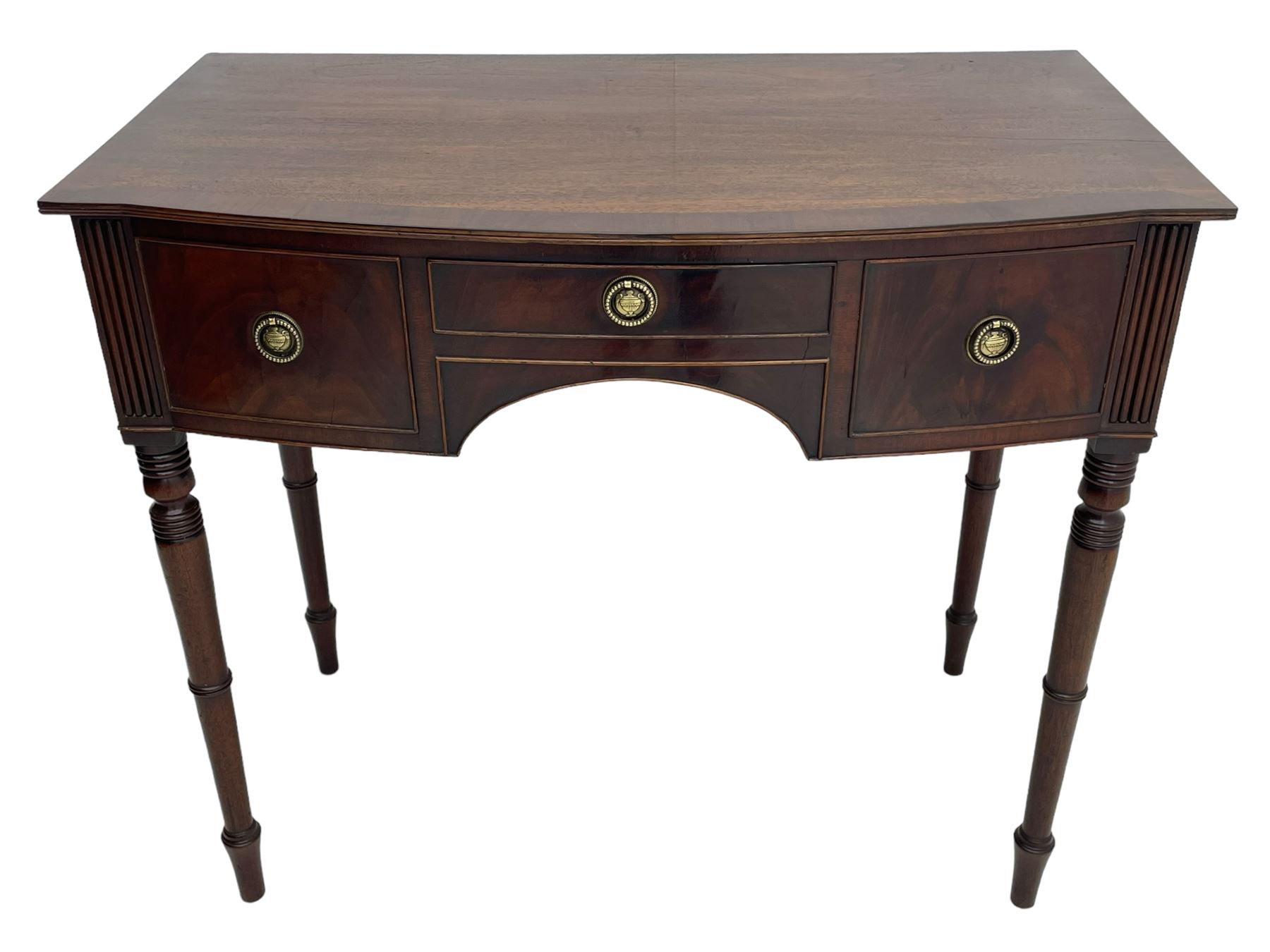 George III mahogany kneehole dressing or writing table, stepped bow-front form, reed moulded top with mahogany crossband, fitted with three cock-beaded drawers with circular pressed brass handle plates decorated with urn and beaded ring handle, on ring turned supports 