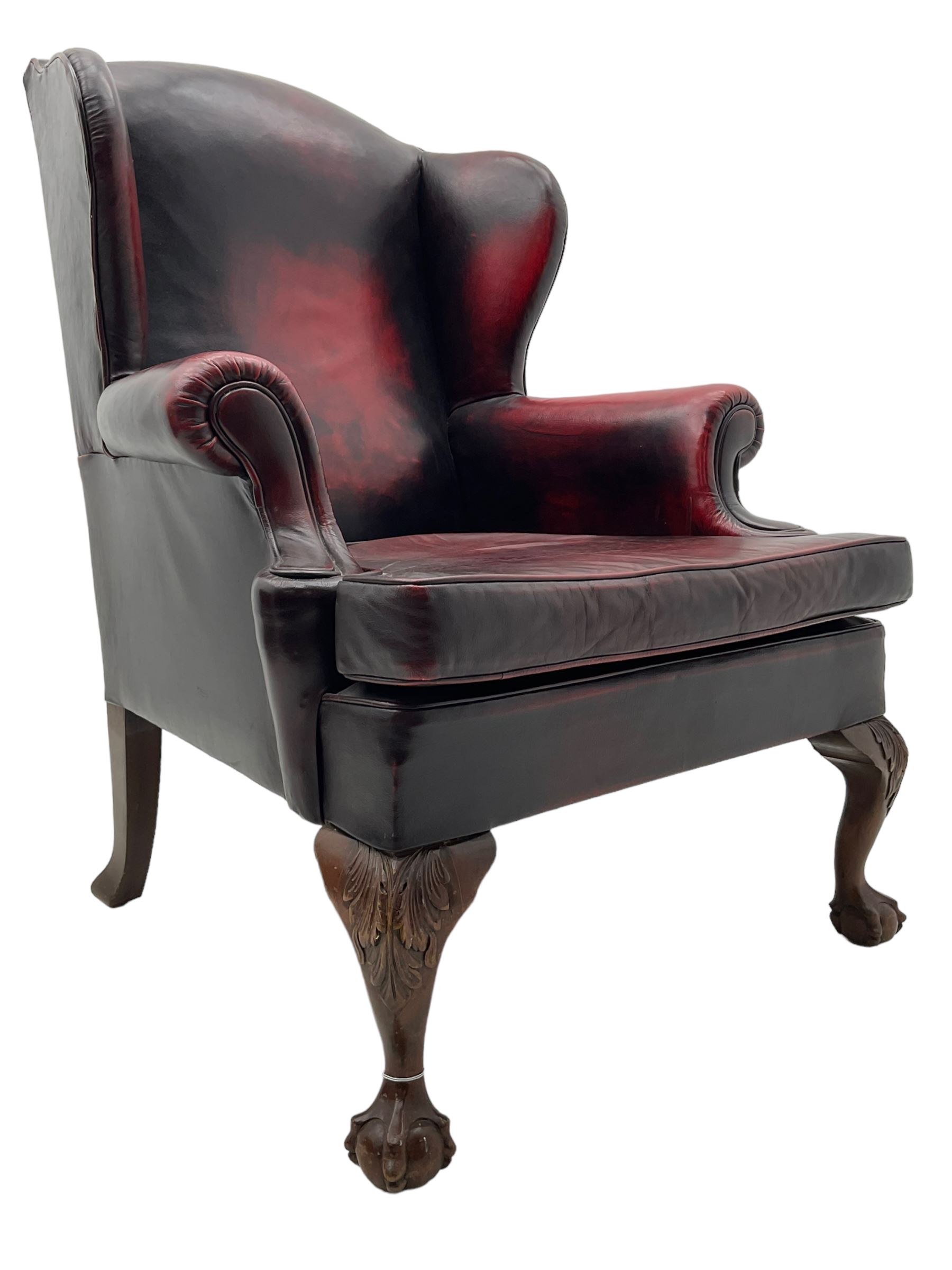 Georgian design hardwood-framed wingback armchair, upholstered in red leather, loose seat cushion and rolled arms, on acanthus carved ball and claw front feet 