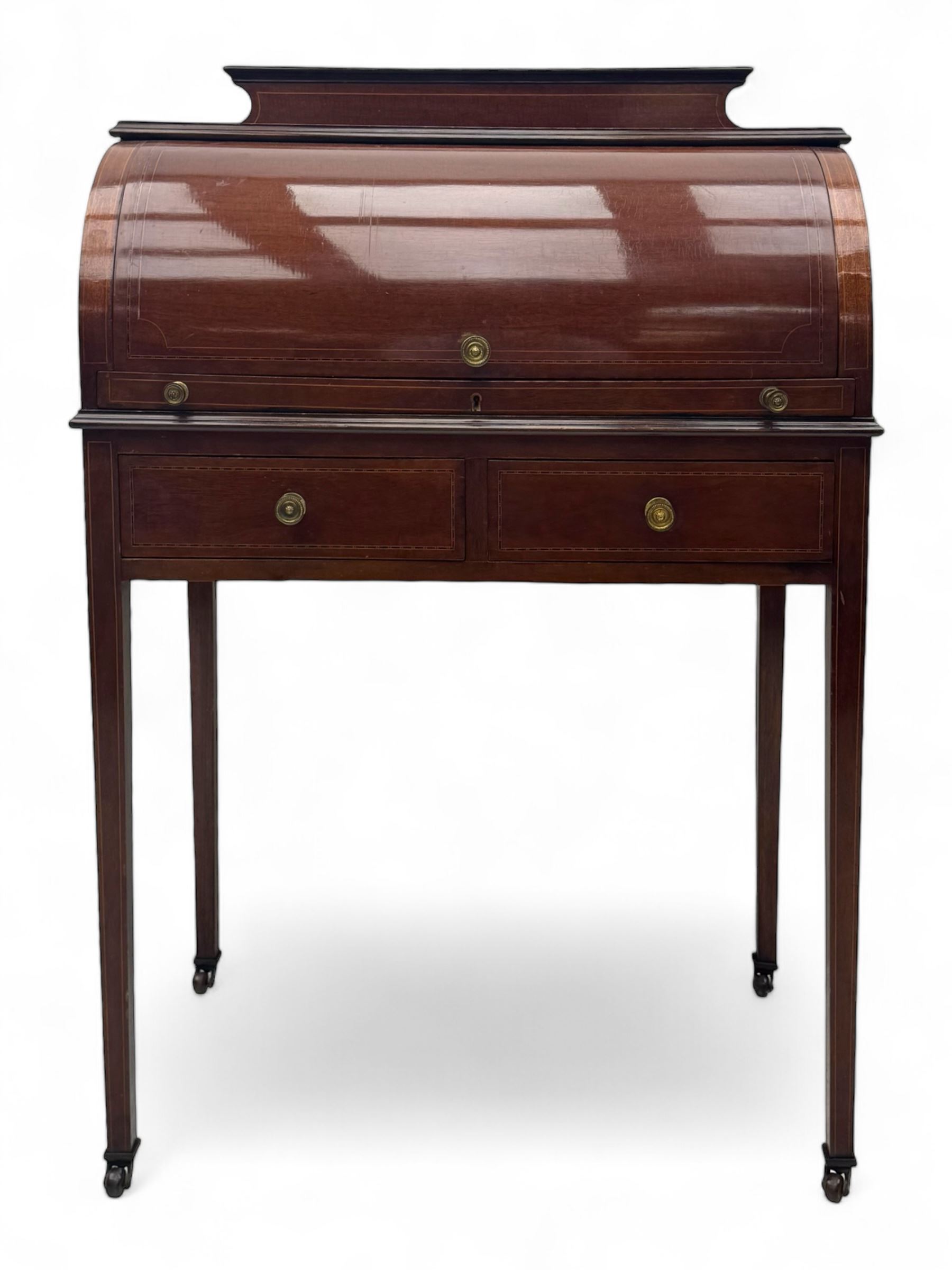 Edwardian inlaid mahogany roll-top desk, cylindrical lid enclosing fitted interior with pigeonholes, drawers and retractable writing surface, over two drawers with brass pull handles, on tapered supports with brass and ceramic castors