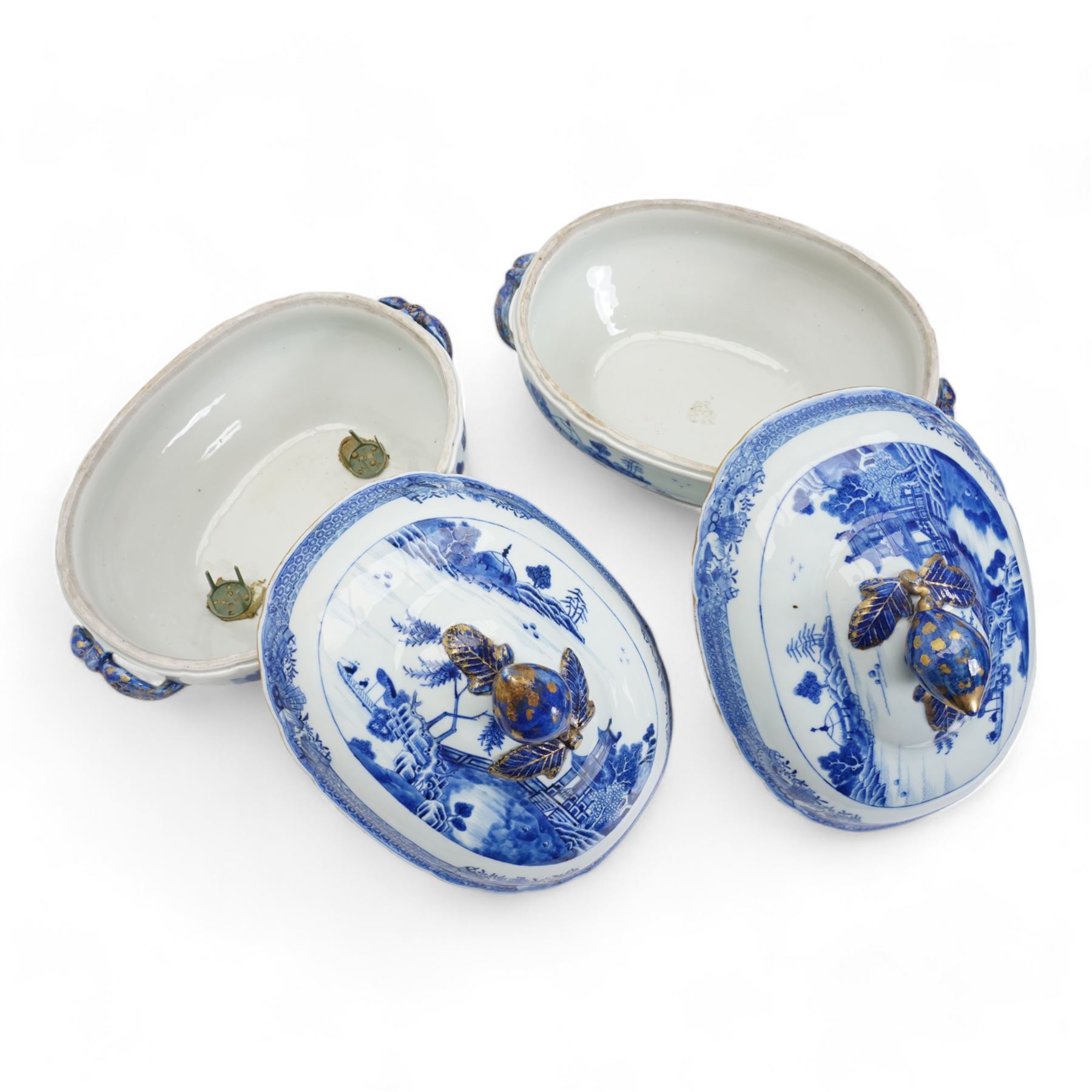 Pair of 18th century Chinese Export blue and white parcel gilt lidded tureens, each of twin handled oval form, decorated with buildings and landscape scenes within geometric and cell borders, with fruit finials, L33cm x H26cm approx.