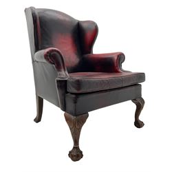 Georgian design hardwood-framed wingback armchair, upholstered in red leather, loose seat cushion and rolled arms, on acanthus carved ball and claw front feet 