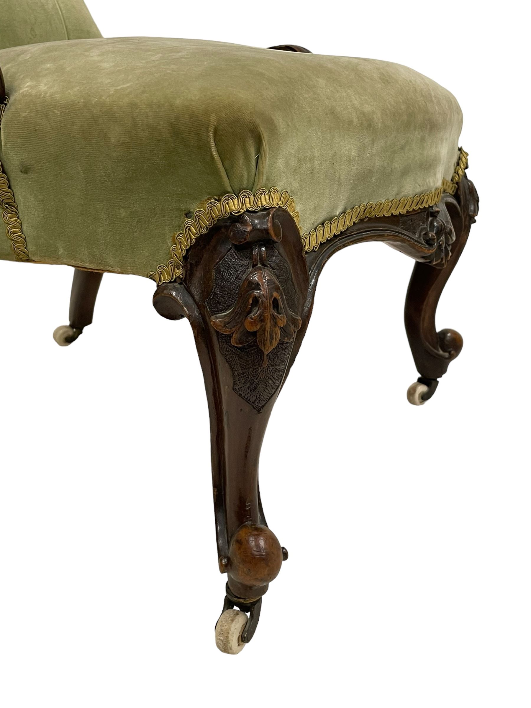 Pair of lady's and gentleman's Victorian carved walnut armchair and nursing chair, foliate carved cresting rail over shaped back with scrolled acanthus carved sides, the armchair with scroll arm terminals, the spoon back and sprung seat upholstered in buttoned sage green velvet, raised on cabriole supports with bell-flower moulded knees and scroll feet, on ceramic castors