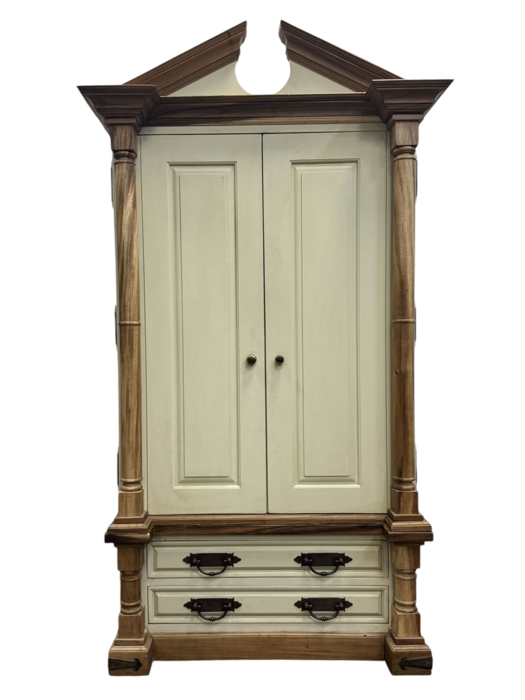 Hardwood and cream painted kitchen larder cupboard, sloped pediment over two panelled doors, the interior fitted with slides, drawers and storage shelves, two long drawers below, mounted by turned pilasters, on metal bound moulded plinth base