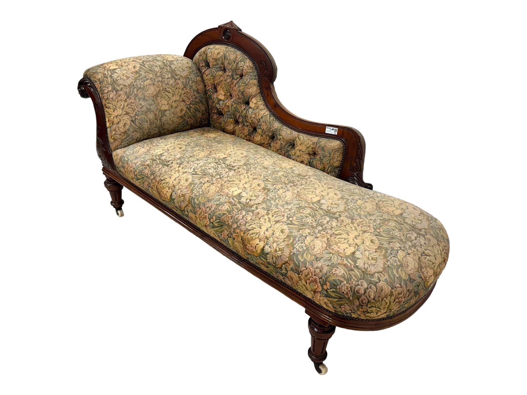 Victorian Aesthetic Movement mahogany framed chaise longue, shaped carved back over acanthus scrolled arm terminal, upholstered in floral patterned tapestry fabric with sprung seat, on turned and fluted supports with castors