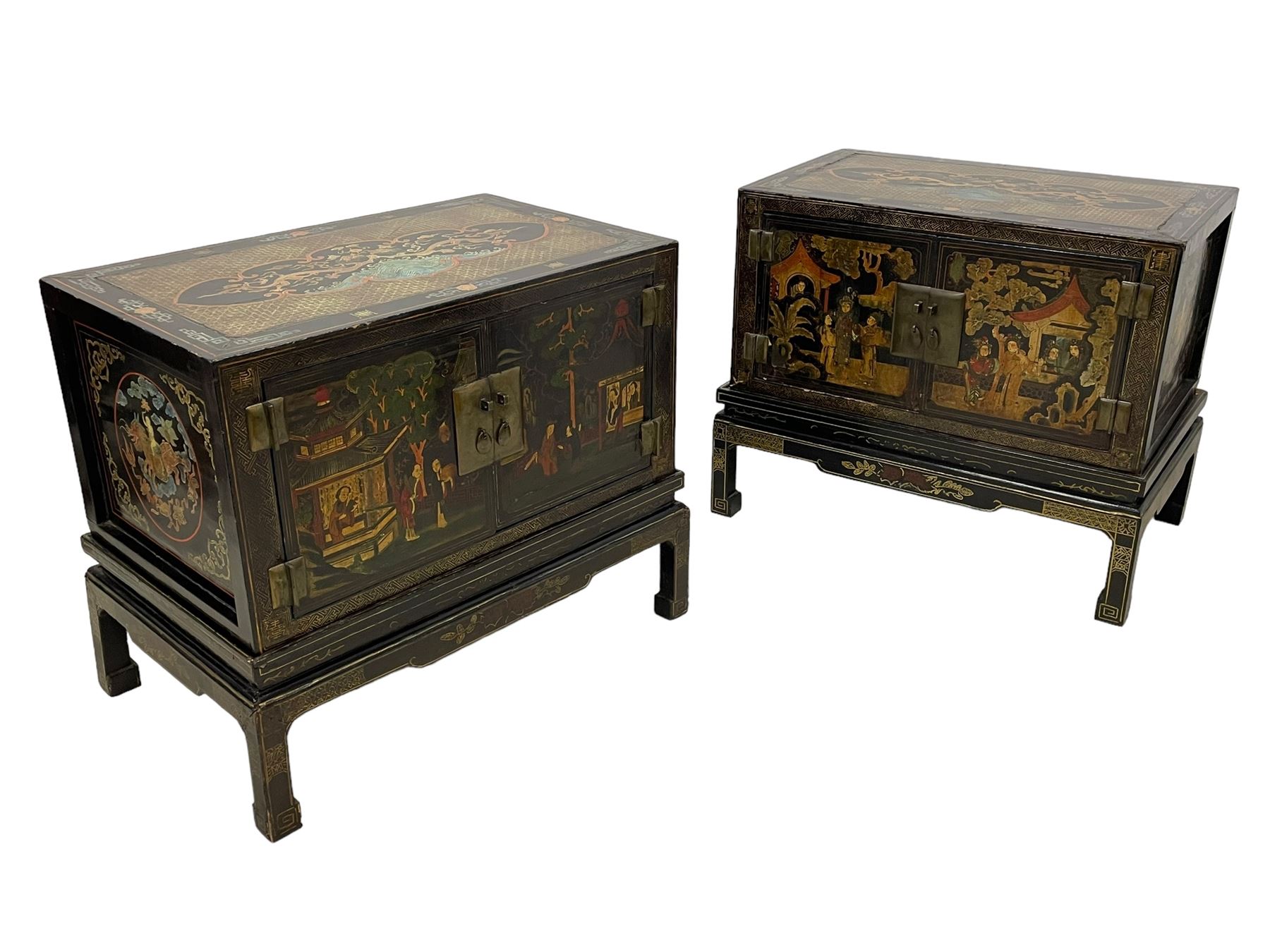 Pair of early 20th century Chinese ebonised and lacquered wood cabinets, the top decorated with dragons over lapping waves within a gilt patterned panel, the surrounding band decorated with Chinese symbols and flowerheads, enclosed by two doors each with village scenes with pagodas, figures and trees, the panelled sides decorated with a figure riding a dragon on stands with gilt decorated 