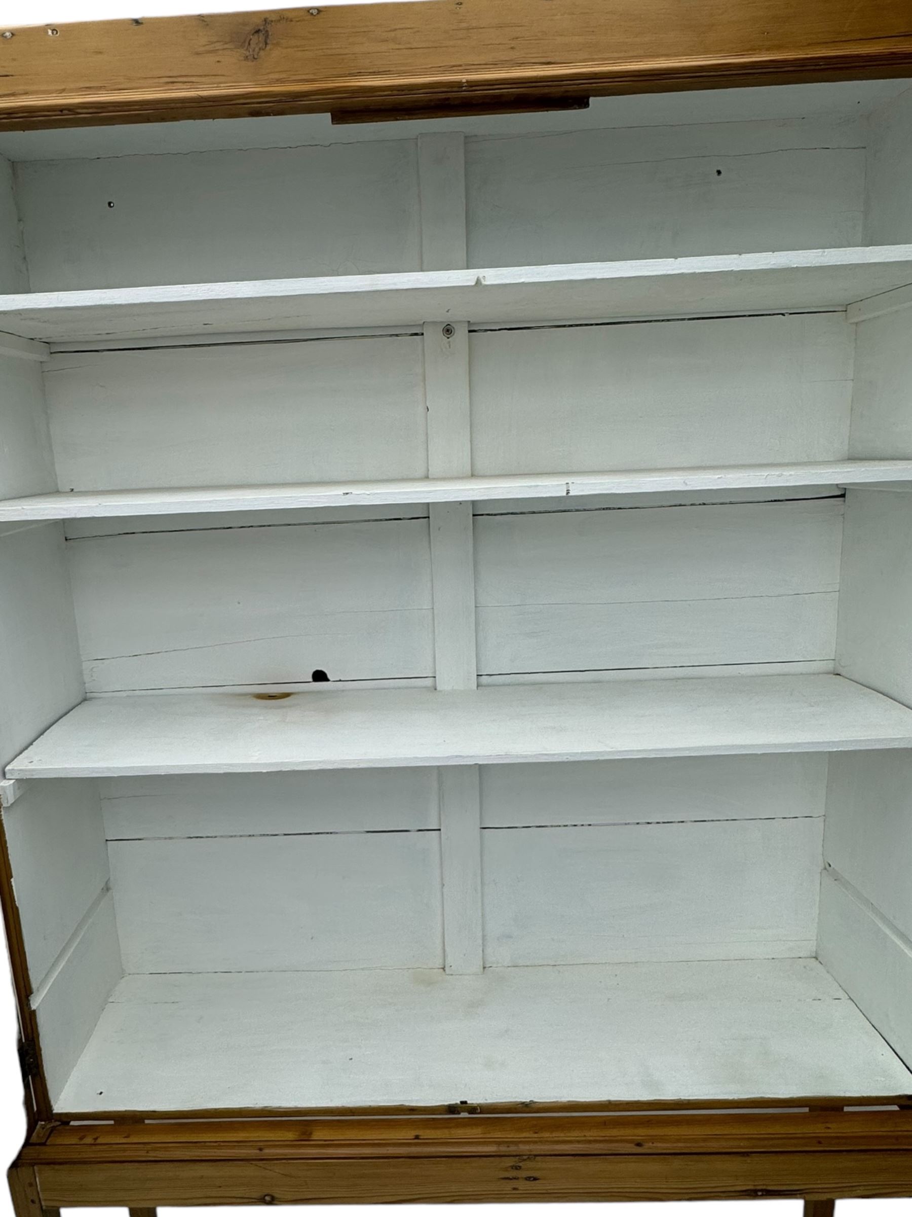 Georgian stripped pine bookcase display cabinet, plain moulded cornice over two glass-panel doors with multiple panes, enclosing white painted interior with three shelves, raised on square supports