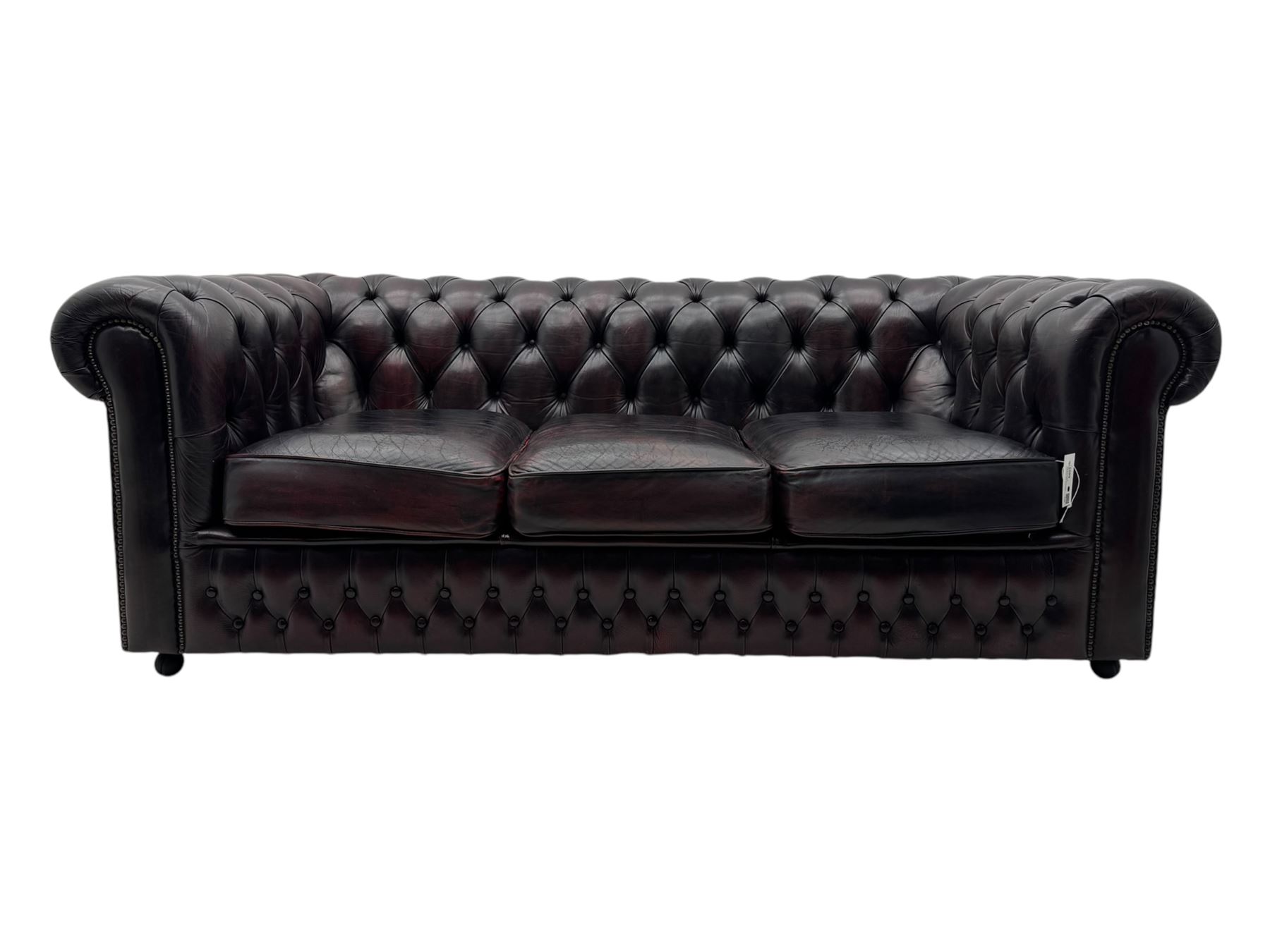 Chesterfield three-seat sofa, traditional shaped upholstered in deeply buttoned dark red leather; together with similar footstool 