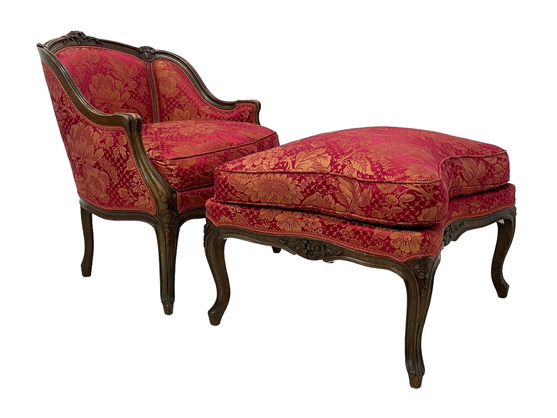 Late 20th century French design stained beech framed armchair and matching stool - the armchair with shaped and moulded frame carved with flower heads and foliage, upholstered in silk red and gold ground fabric with floral pattern, on scroll carved cabriole feet decorated with flower head carvings (W73cm, H82cm, D75cm); the footstool of concaved rectangular form with moulded frame carved with flower heads, upholstered loose cushion, on cabriole feet (70cm x 64cm, H48cm)