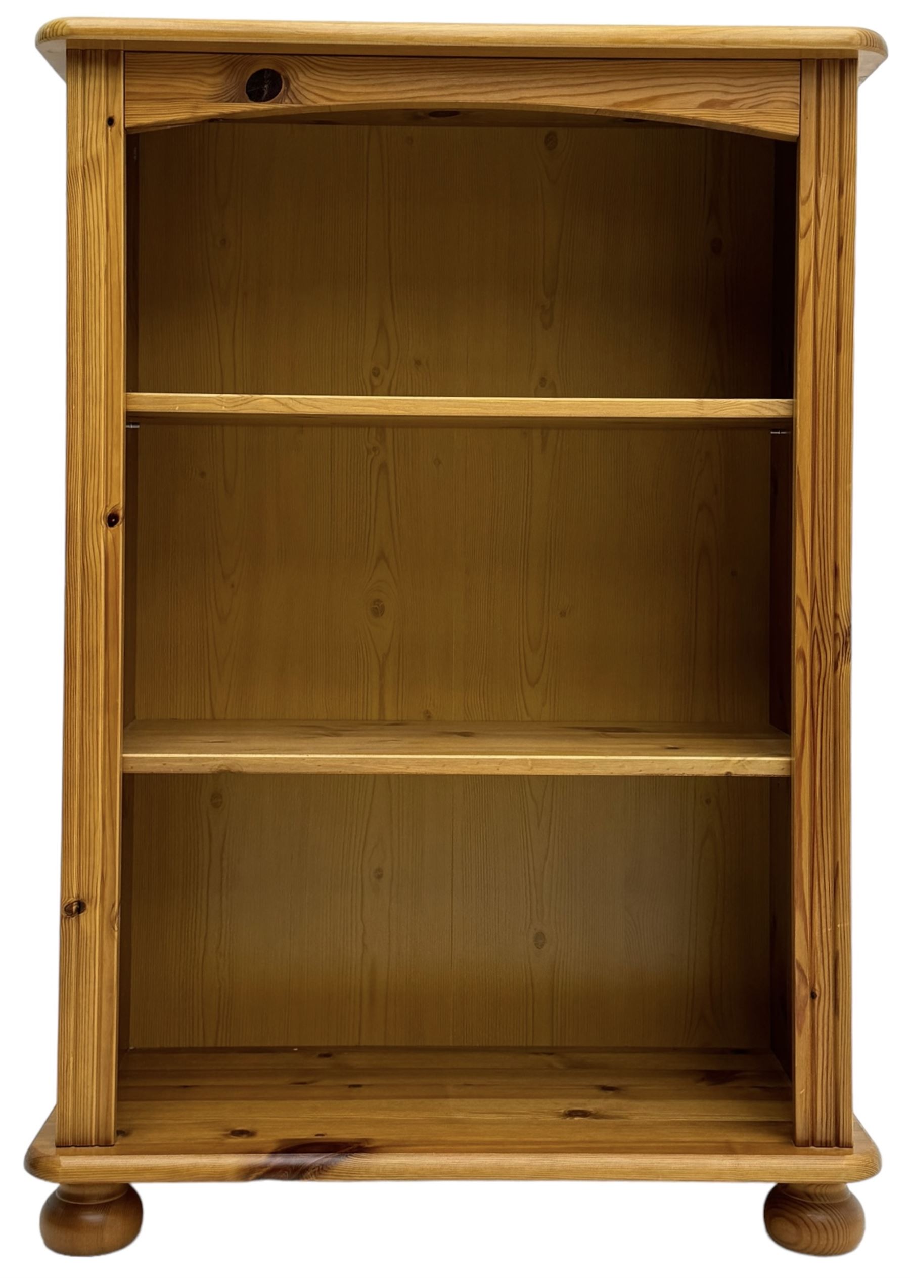 Traditional pine open bookcase, featuring arched top section flanked by fluted side supports, two adjustable shelves and cast iron coat hook with cat motif to the left side, standing on round bun feet 