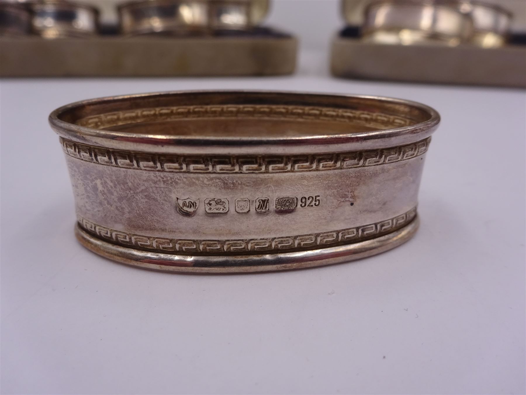 Two sets of six modern silver napkin rings, each of oval form, with Greek key decoration, hallmarked Ari D Norman, London 1986, both in fitted cases