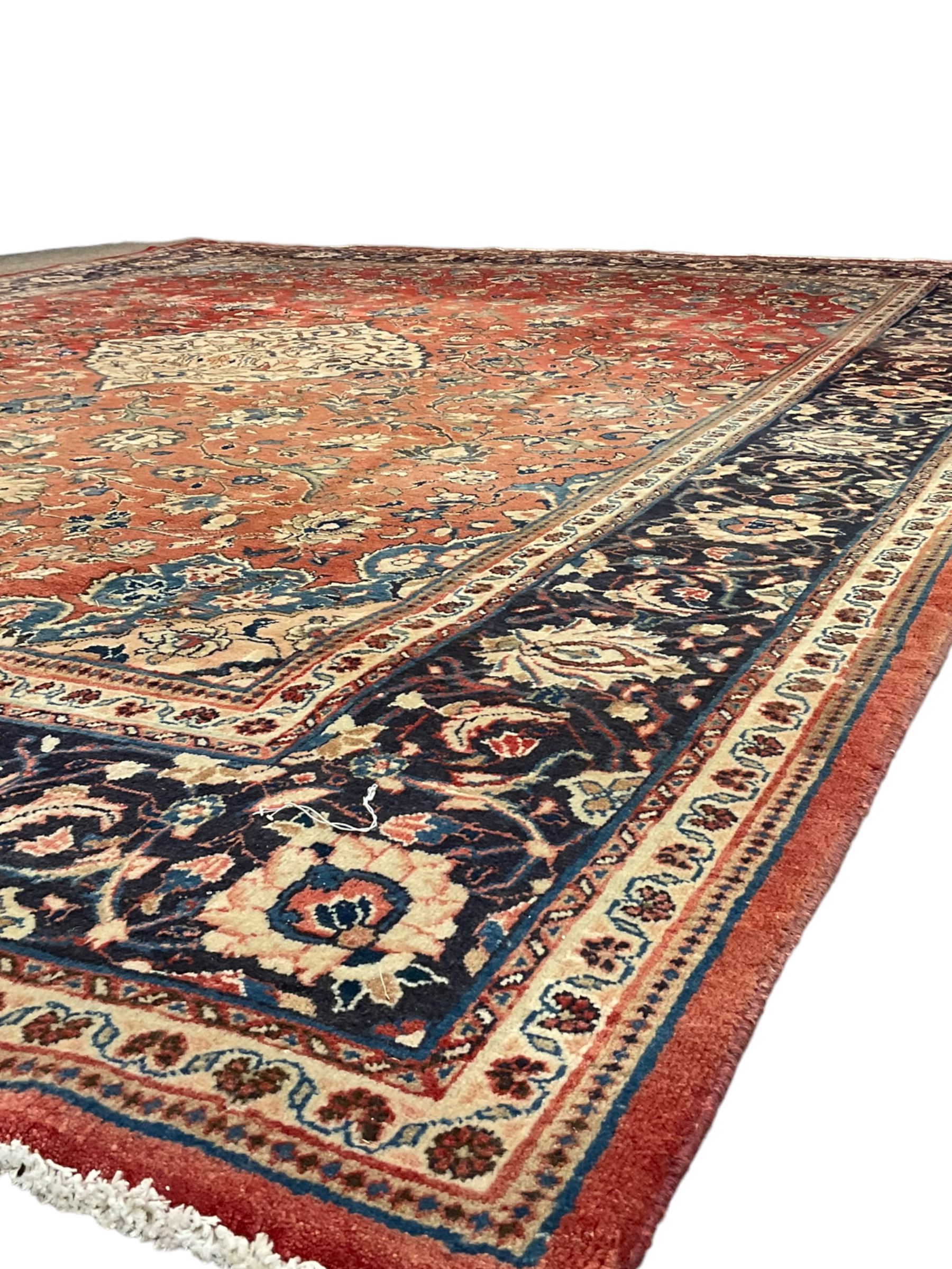 Persian Kashan crimson ground carpet, central shaped pale ground medallion surrounded by interlacing branches and stylised floral motifs, indigo main border with scrolling foliage design, within guard stripes 