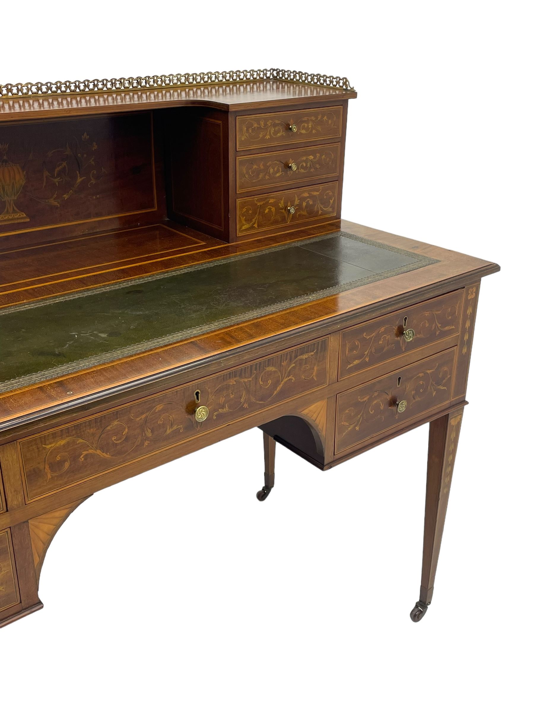 Edwardian inlaid mahogany writing desk, raised galleried back over inlaid central urn with scrolling leafy branches and six small drawers, satinwood banded rectangular moulded top with tooled leather inset, fitted with five drawers, the drawer facias inlaid with scrolling foliage and satinwood banding, square tapering supports inlaid with trailing bell flowers, on brass and ceramic castors 